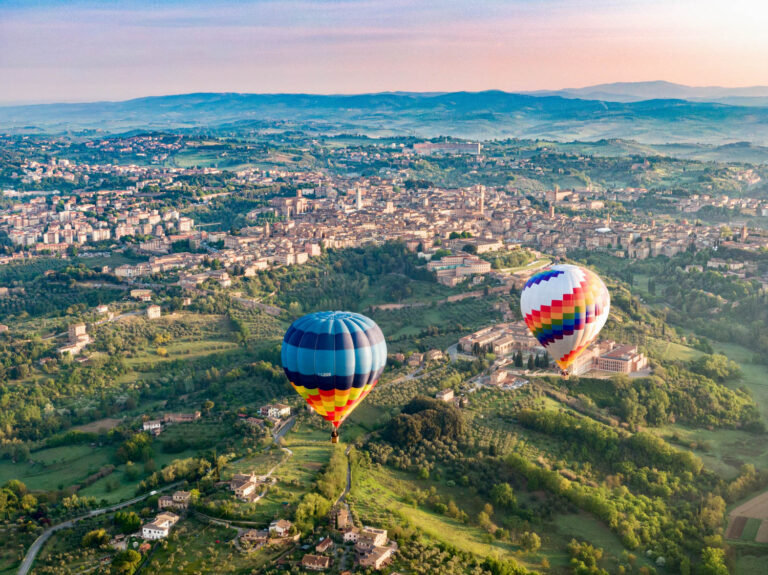Two hot air balloons floating over a hilltop city and green countryside at sunrise