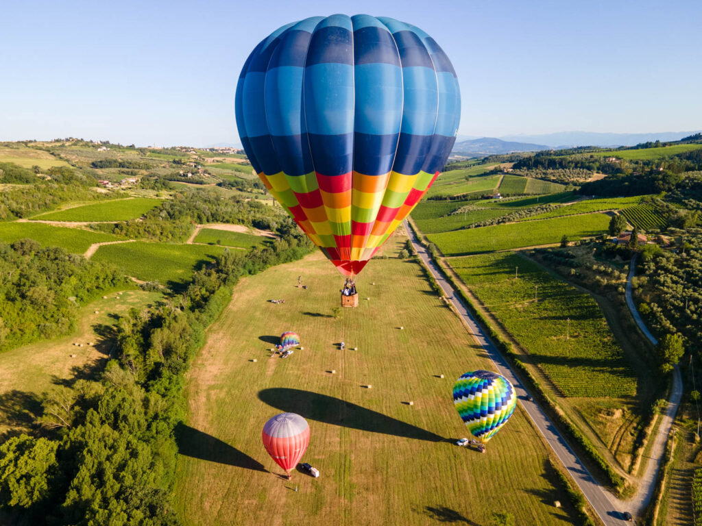 Large striped hot air balloon landing in a meadow with two more balloons among green fields