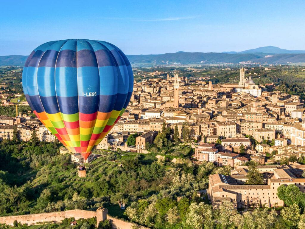 Hot air balloon rising above the terracotta rooftops and towers of Siena