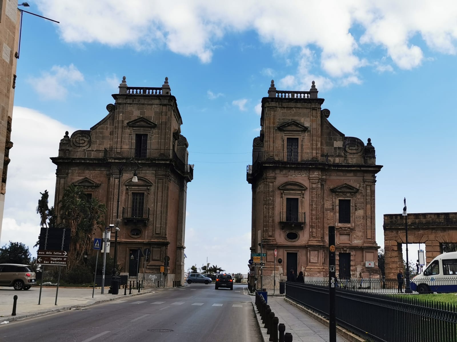 Two weathered stone gate towers framing a wide road under a blue sky