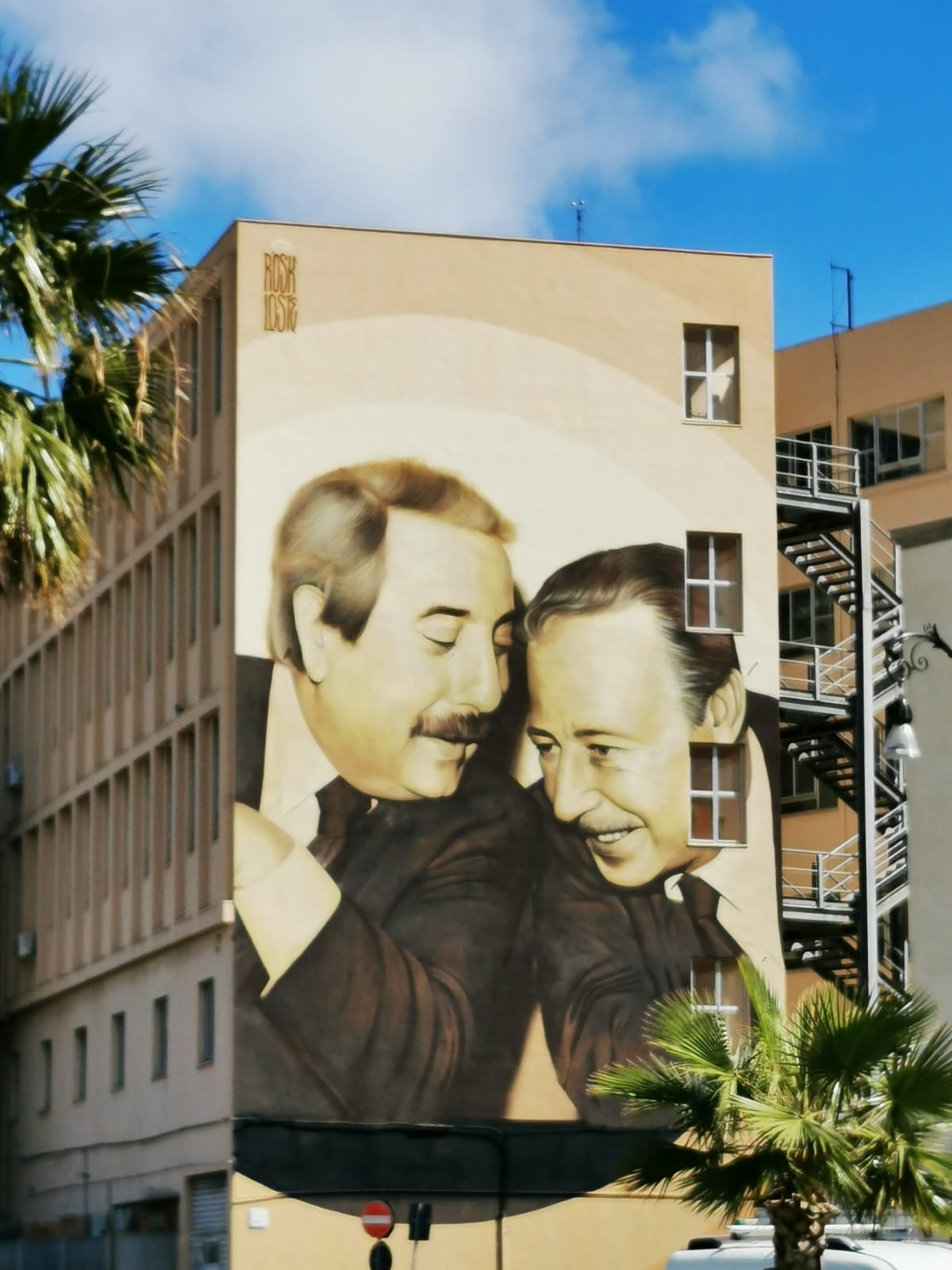 Large wall mural of two smiling men embracing, on the side of an apartment block