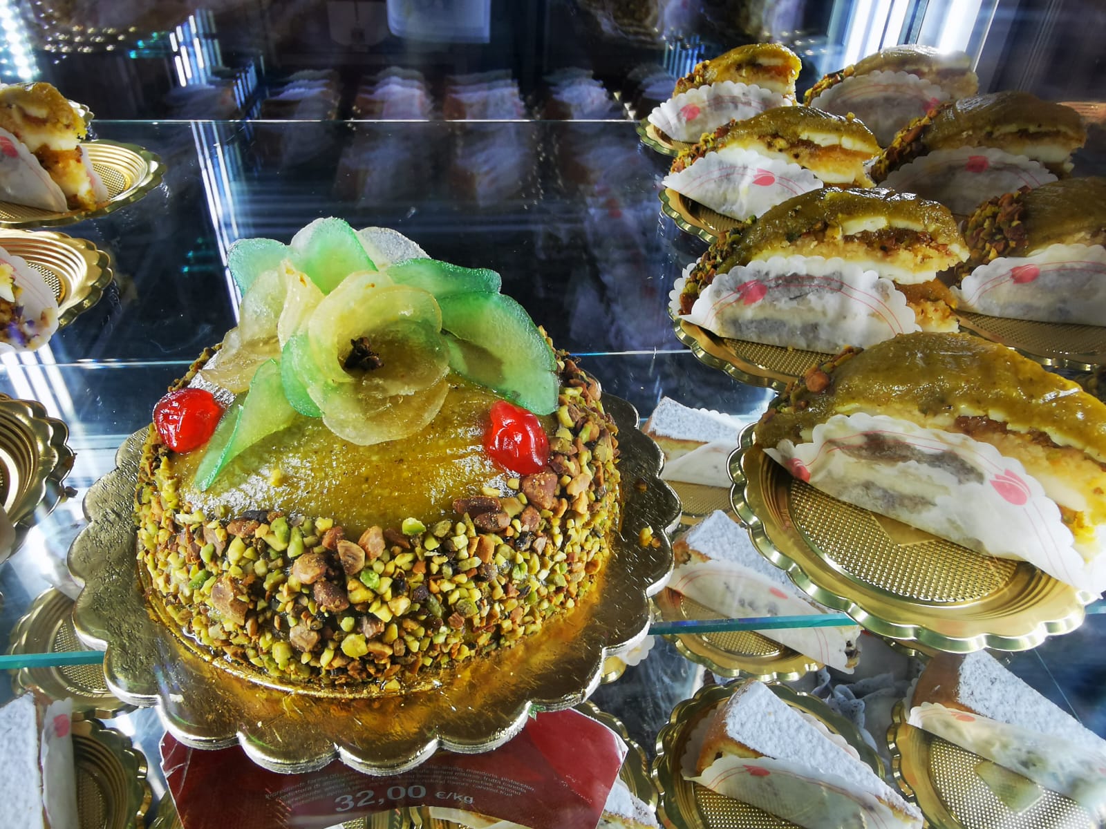 Pistachio-topped Sicilian cake with candied fruit in a pastry shop display case