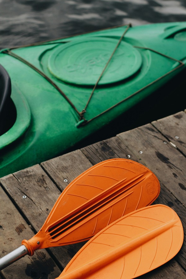 Green kayak moored beside a wooden jetty with two orange paddles resting on the planks
