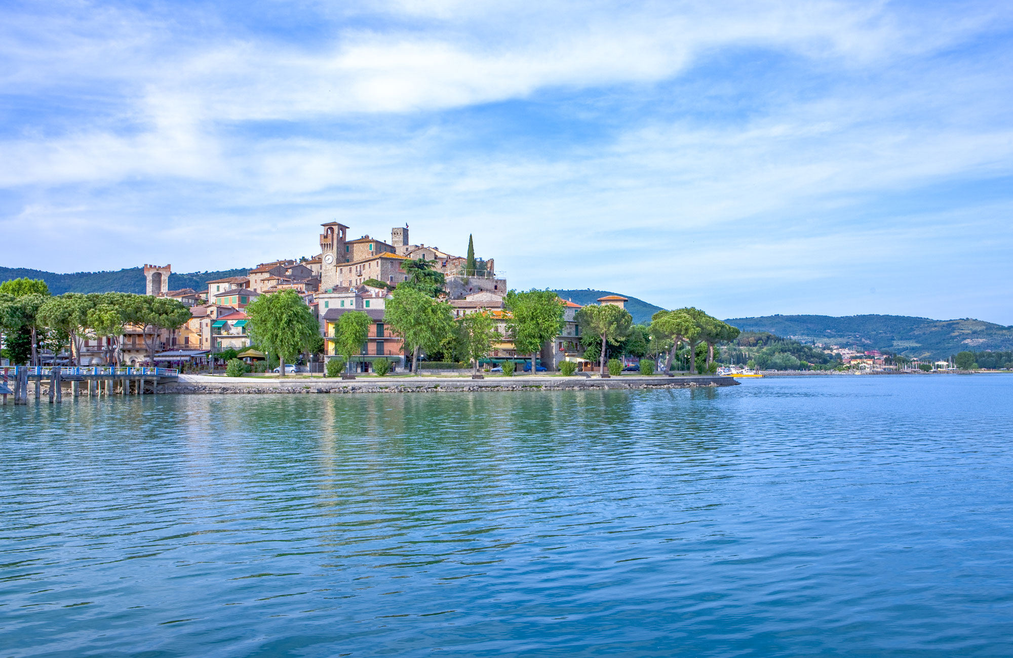 Hill village with a tower on the shore of a calm blue lake in Umbria