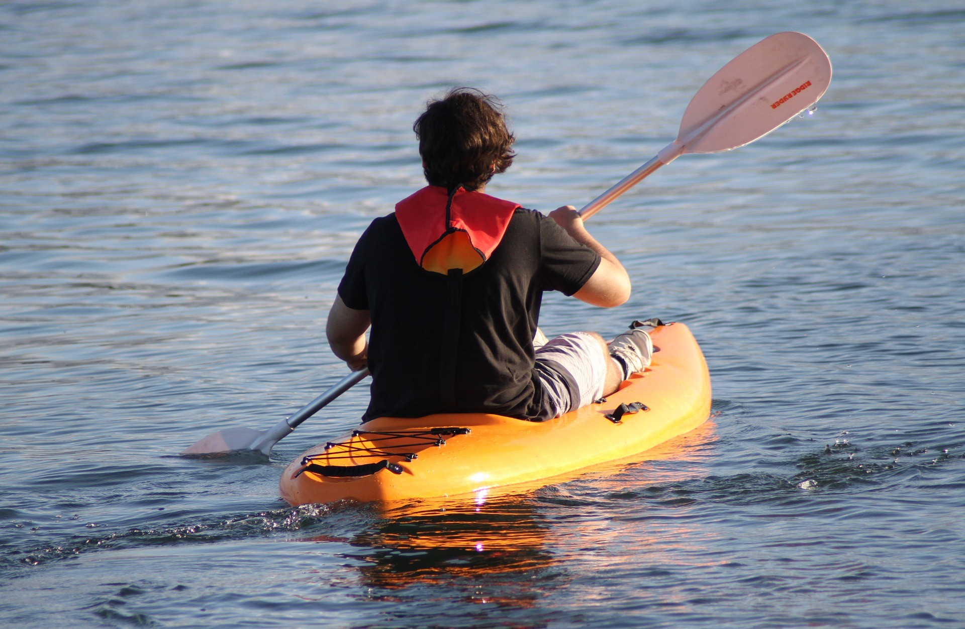 Kayaker in an orange kayak paddling across rippling water at sunset