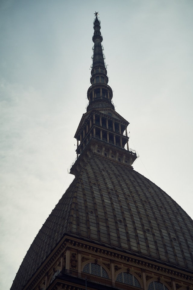 Spire and brick dome of the Mole Antonelliana rising against a pale sky in Turin