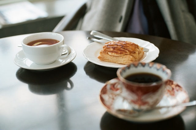 Cup of tea, a flaky pastry and a coffee in a patterned cup on a dark café table