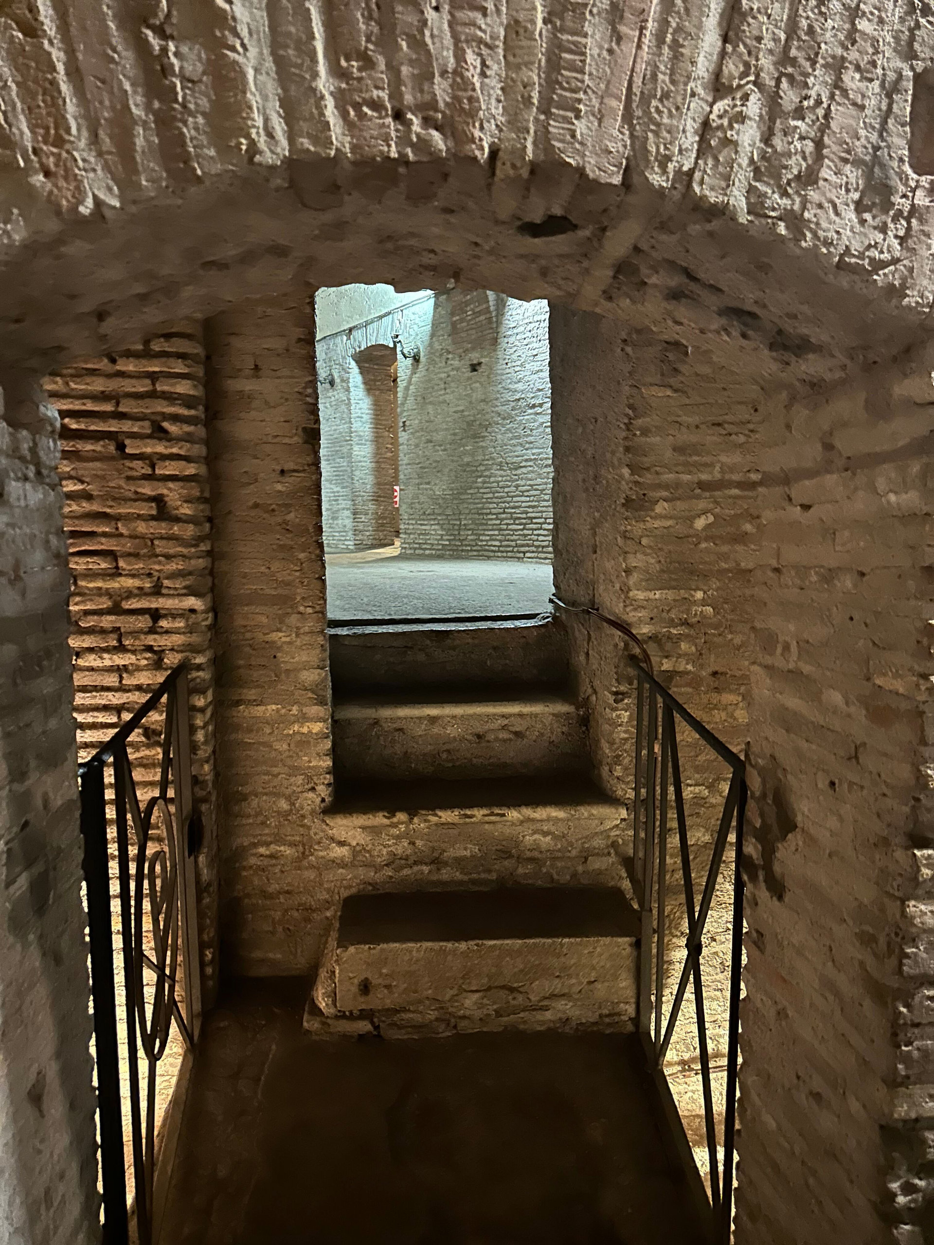 Short stone stairway between brick walls leading to a lower underground chamber