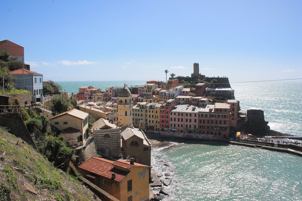 Pastel houses and a bell tower clustered on the rocky shore of a Cinque Terre village above a turquoise sea