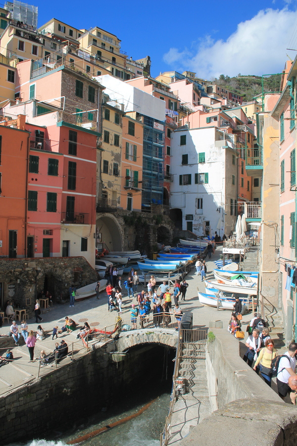 Narrow harbour of a Ligurian village with colourful tall houses, moored boats and strolling visitors
