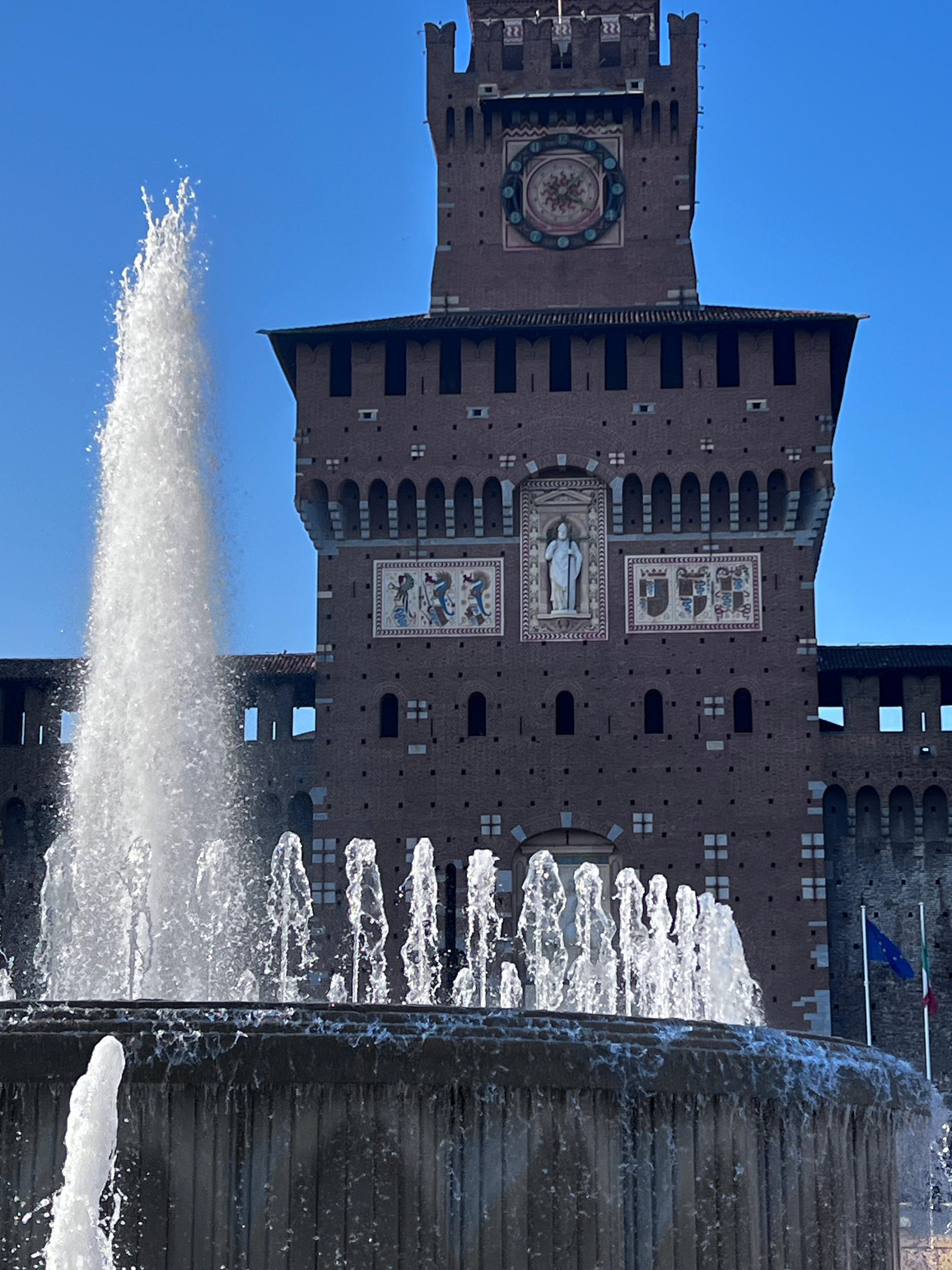 Tower of Sforza Castle in Milan rising behind a splashing fountain