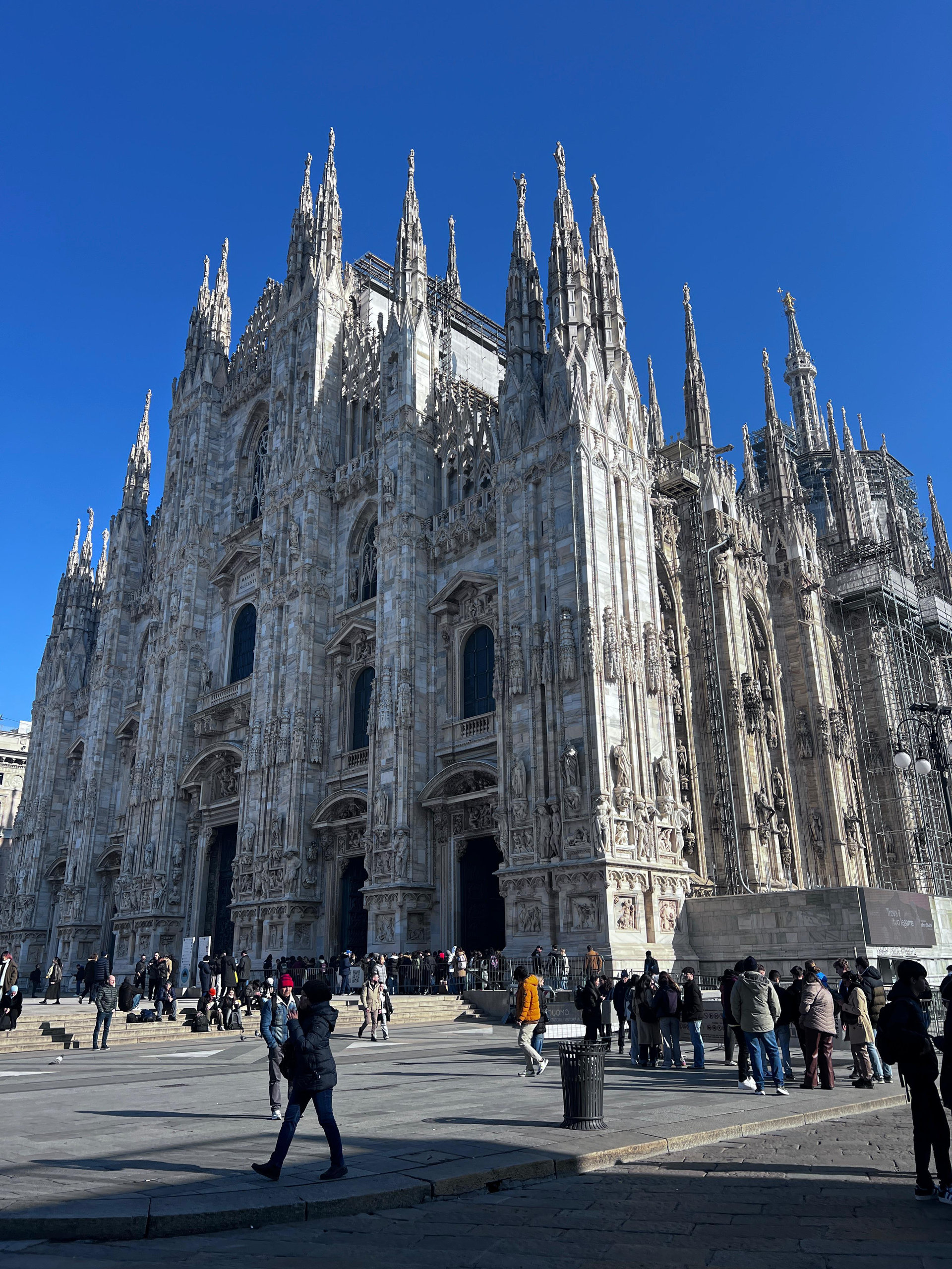 Gothic spires and marble facade of Milan Cathedral with visitors crossing the square