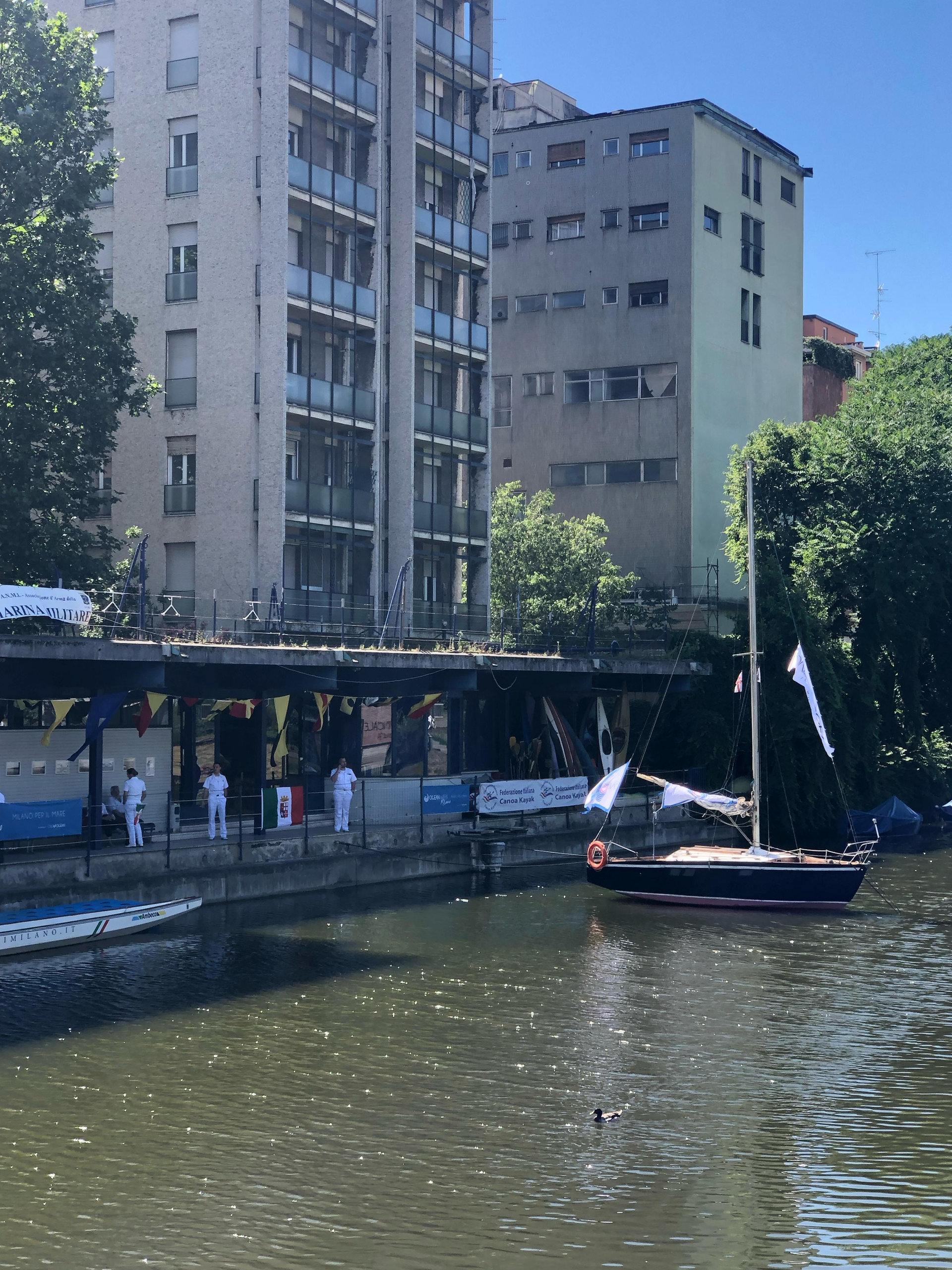 Boat moored on a Milan canal beside modern apartment blocks and trees