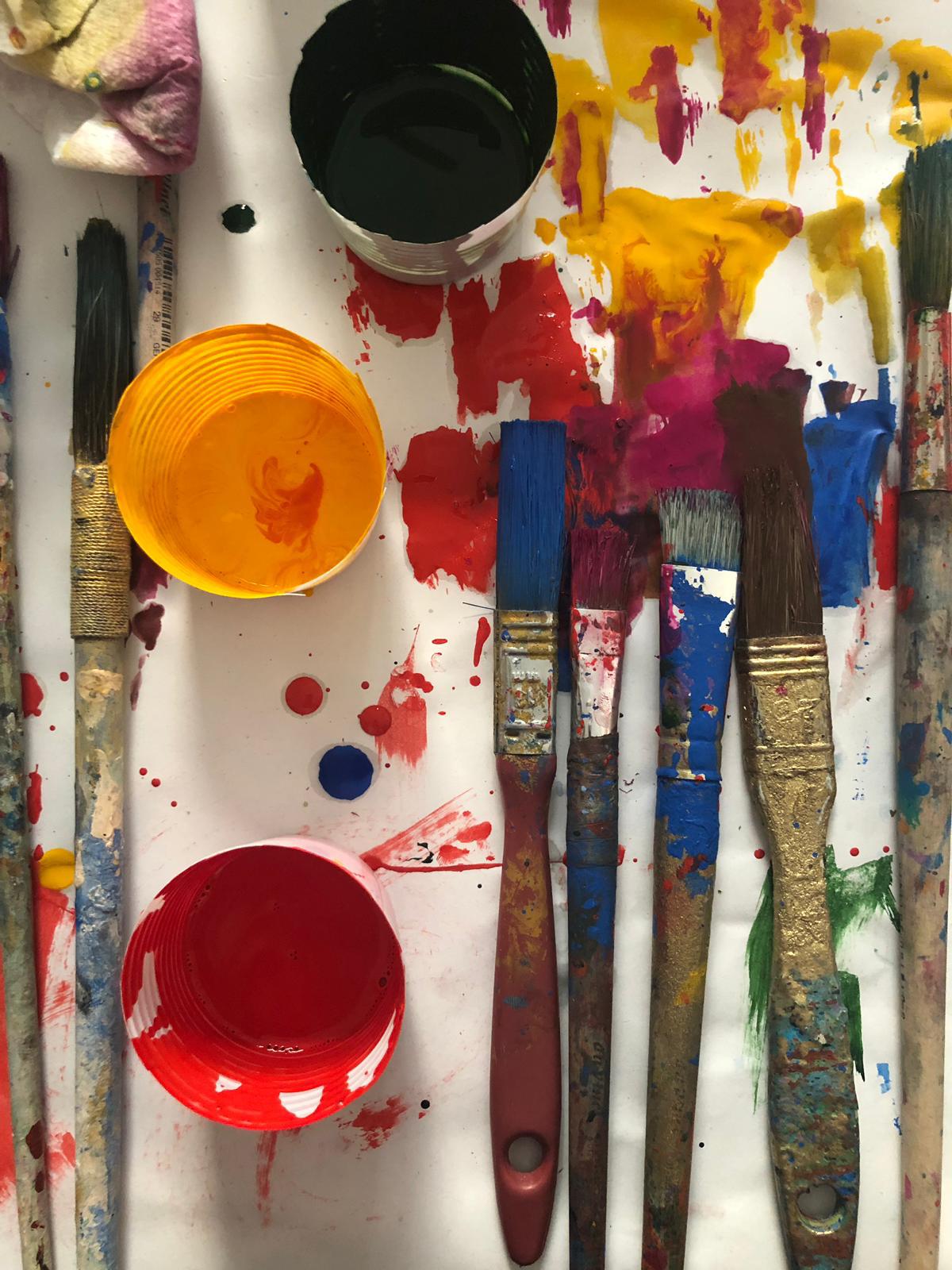 Paint-splattered brushes and pots of red and yellow paint on a sheet of paper