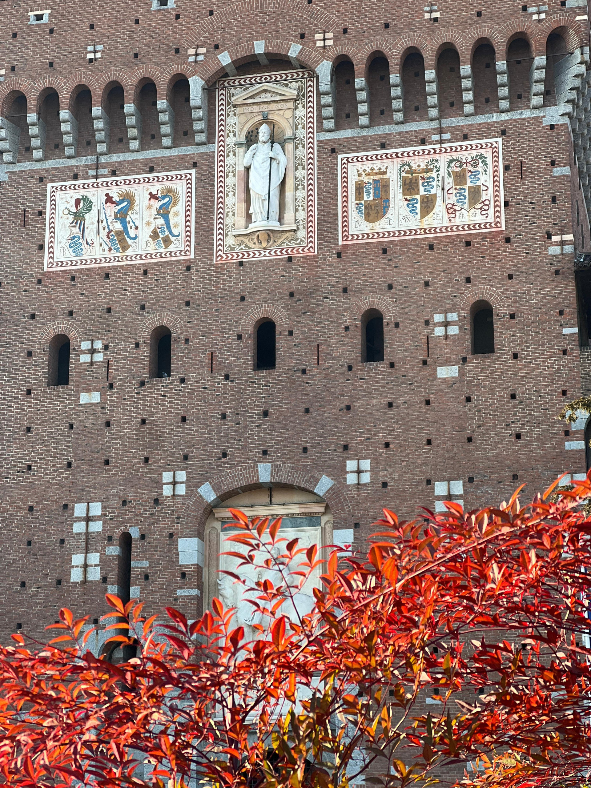 Brick tower of Sforza Castle with carved relief panels framed by red autumn foliage