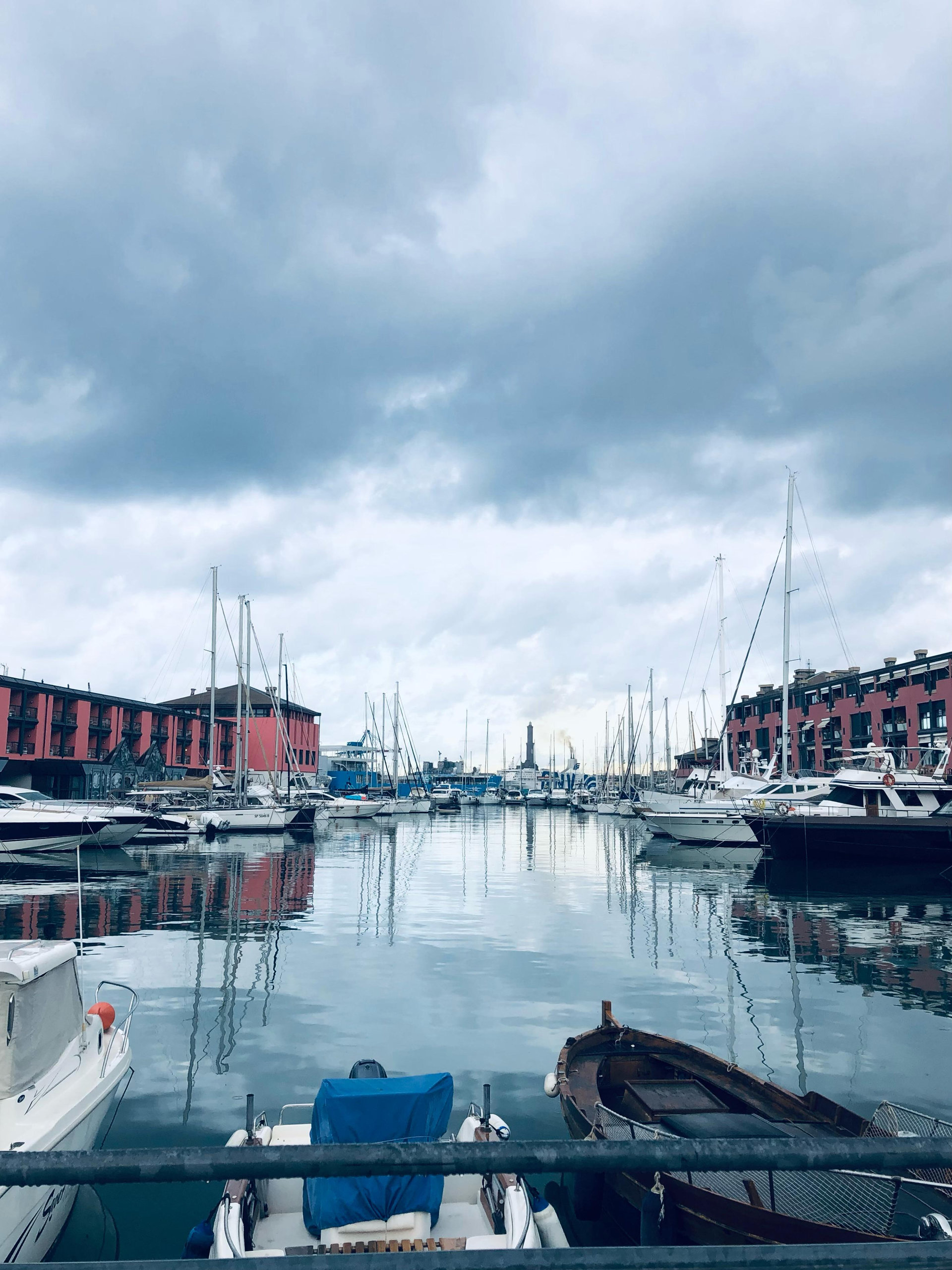 Moored sailing boats in a calm harbour under a cloudy sky, with red brick warehouses