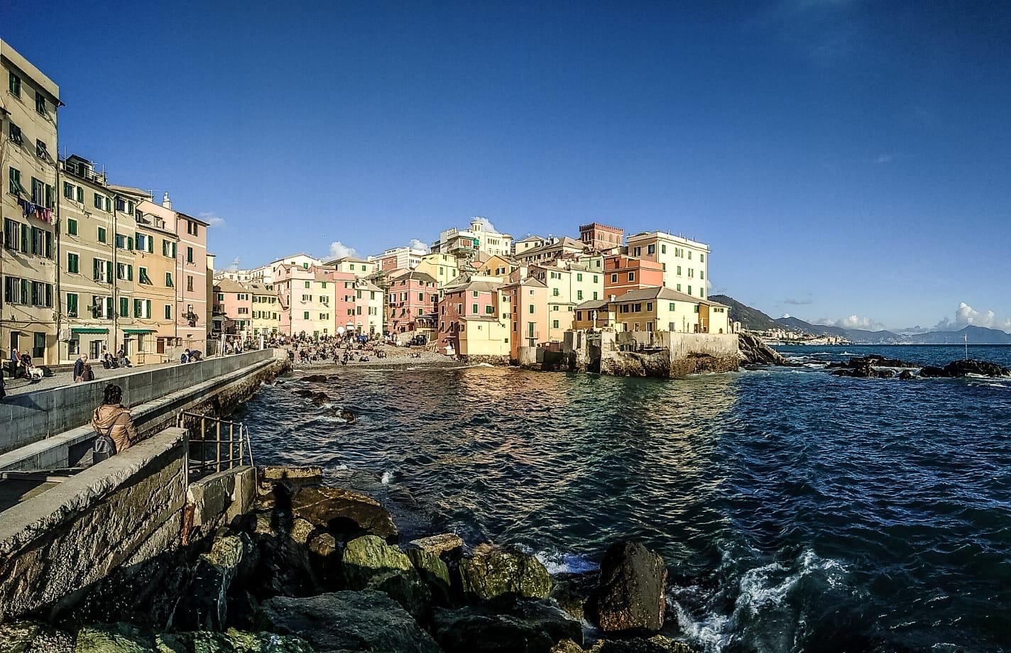 Pastel houses of a seaside village clustered above rocks and a deep blue sea at golden hour