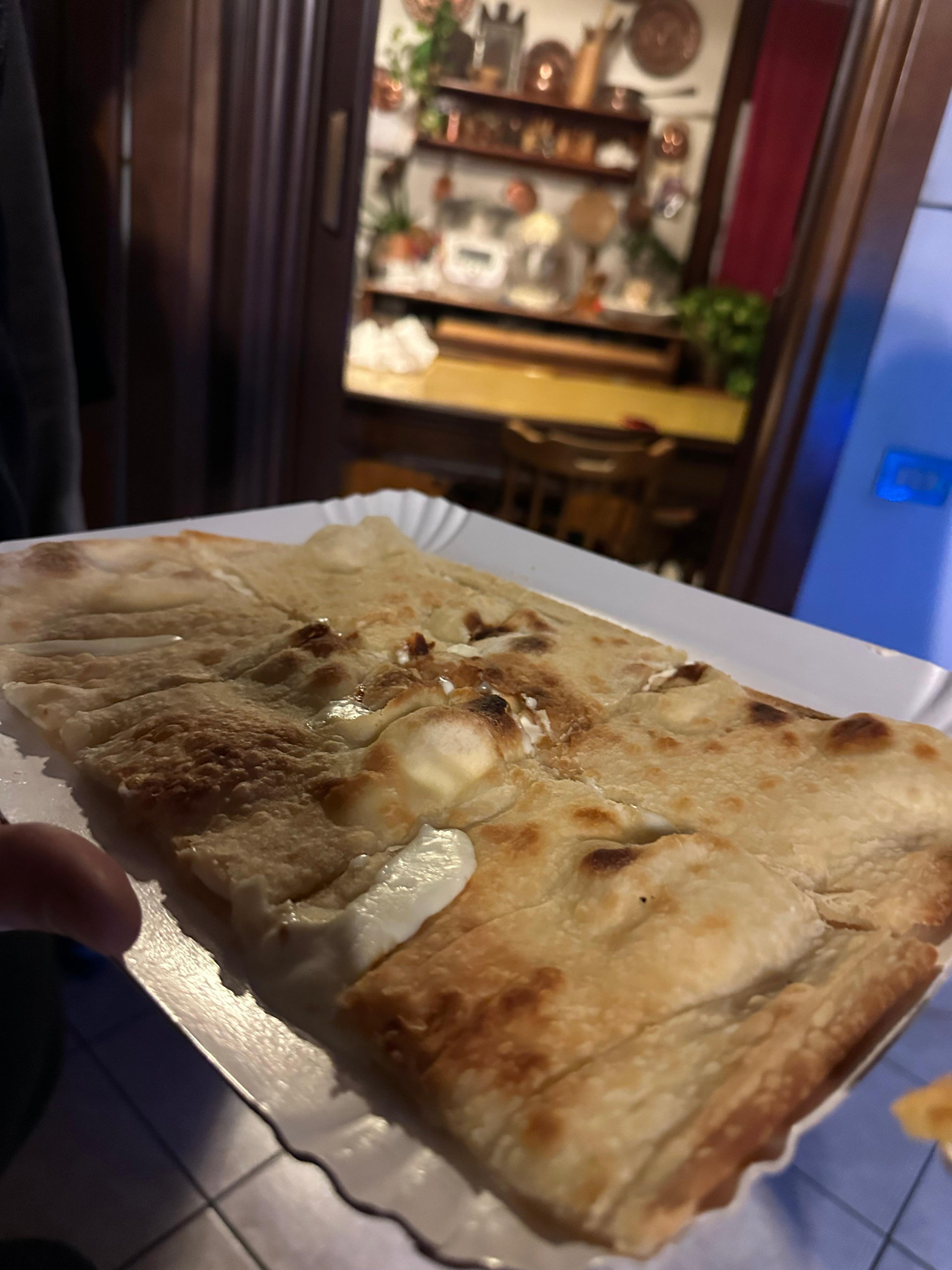 Slice of golden focaccia with melted cheese held on a paper tray