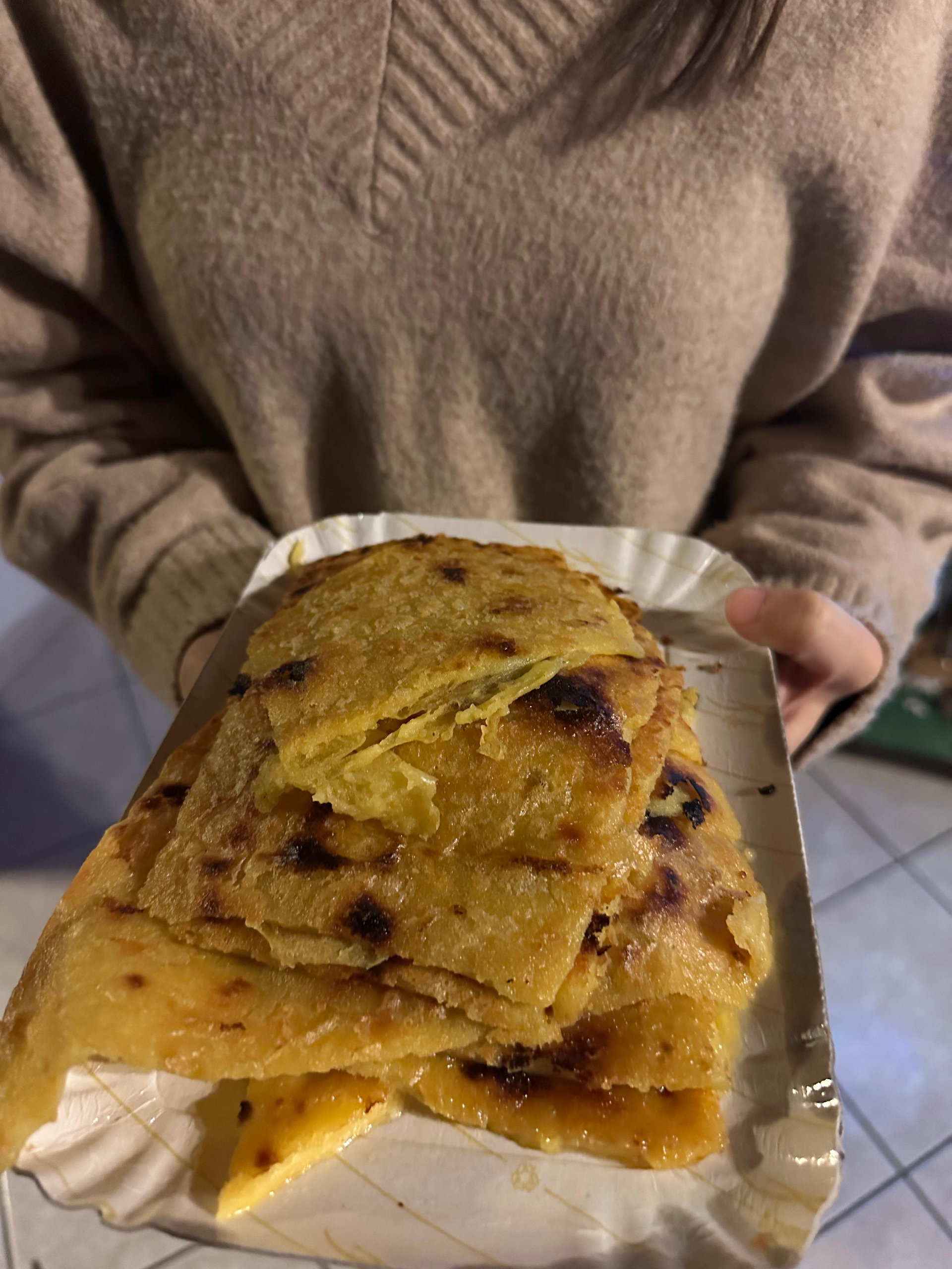 Stack of golden, charred-edged chickpea farinata slices on a paper tray