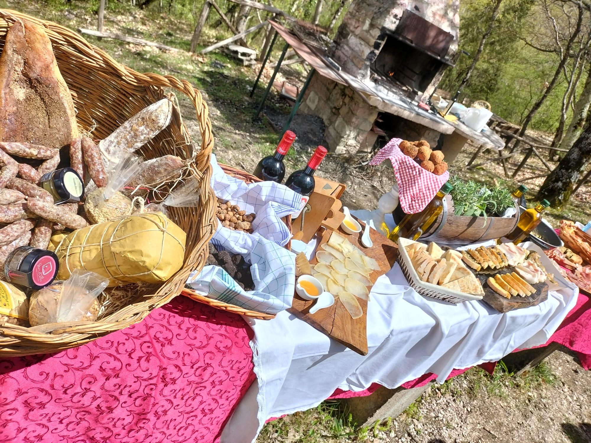 Picnic table laden with cured meats, cheeses, bread and wine beside a stone outdoor oven