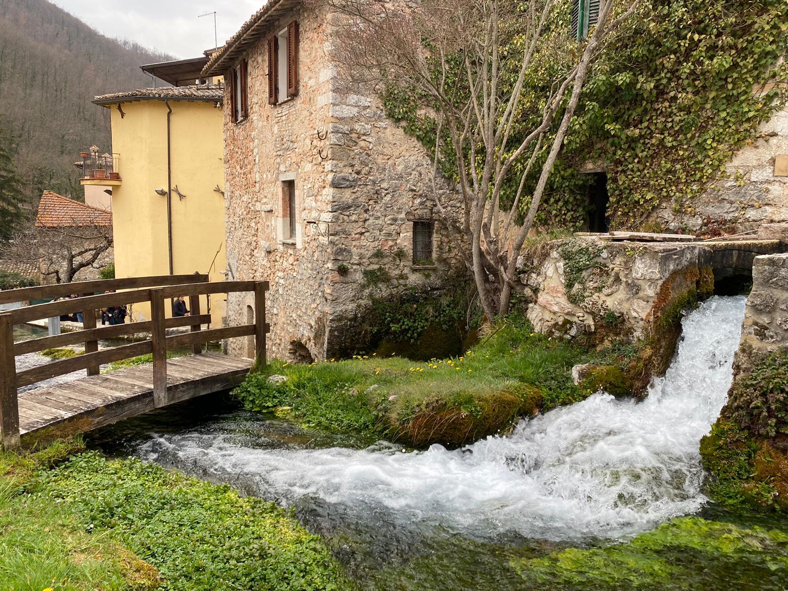 Stone mill house with a wooden footbridge beside a rushing stream