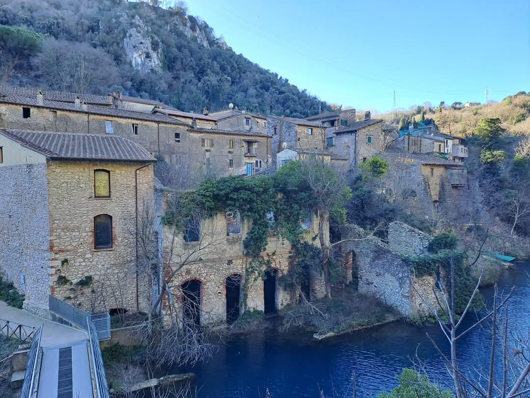 Old stone houses climbing a wooded hillside above a dark blue river