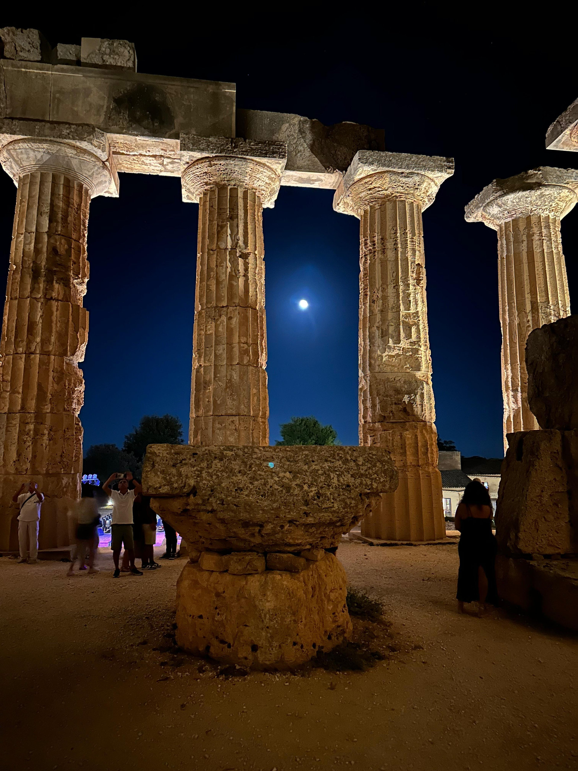Doric columns of a Greek temple lit at night beneath a full moon