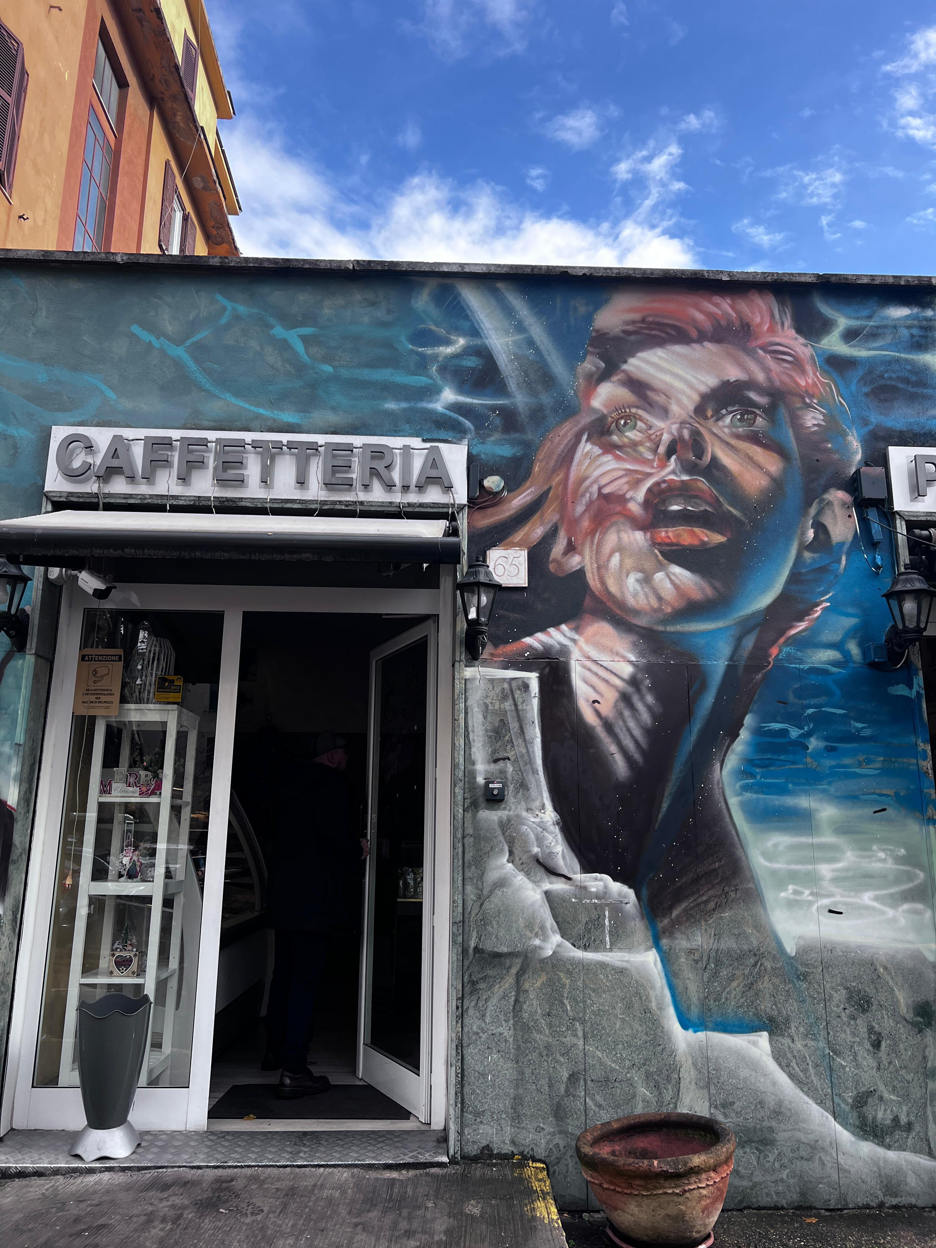 Mural of a woman's face in red and blue tones beside the door of a small caffetteria
