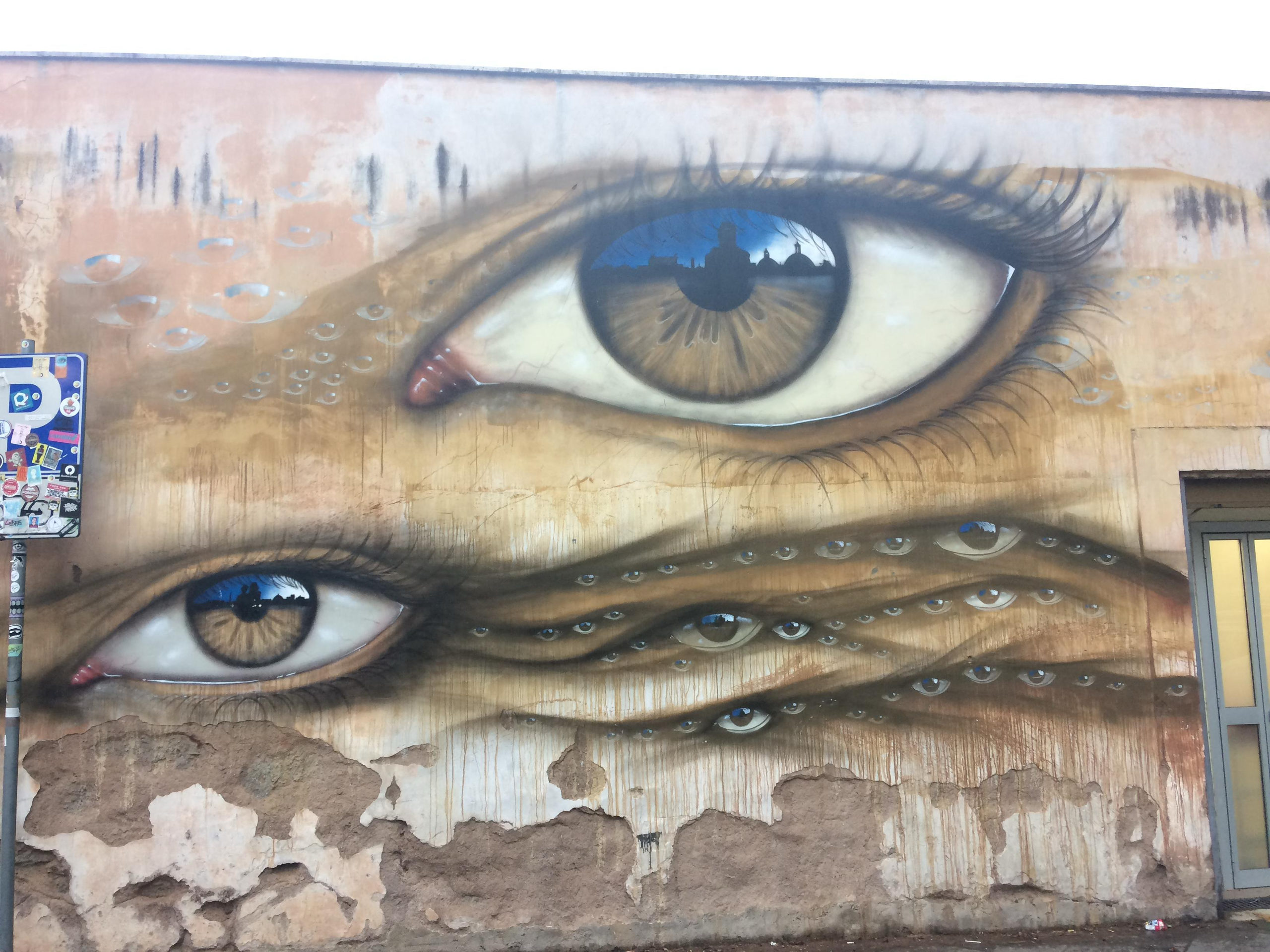 Mural of two large eyes with tiny eyes drifting across a weathered wall