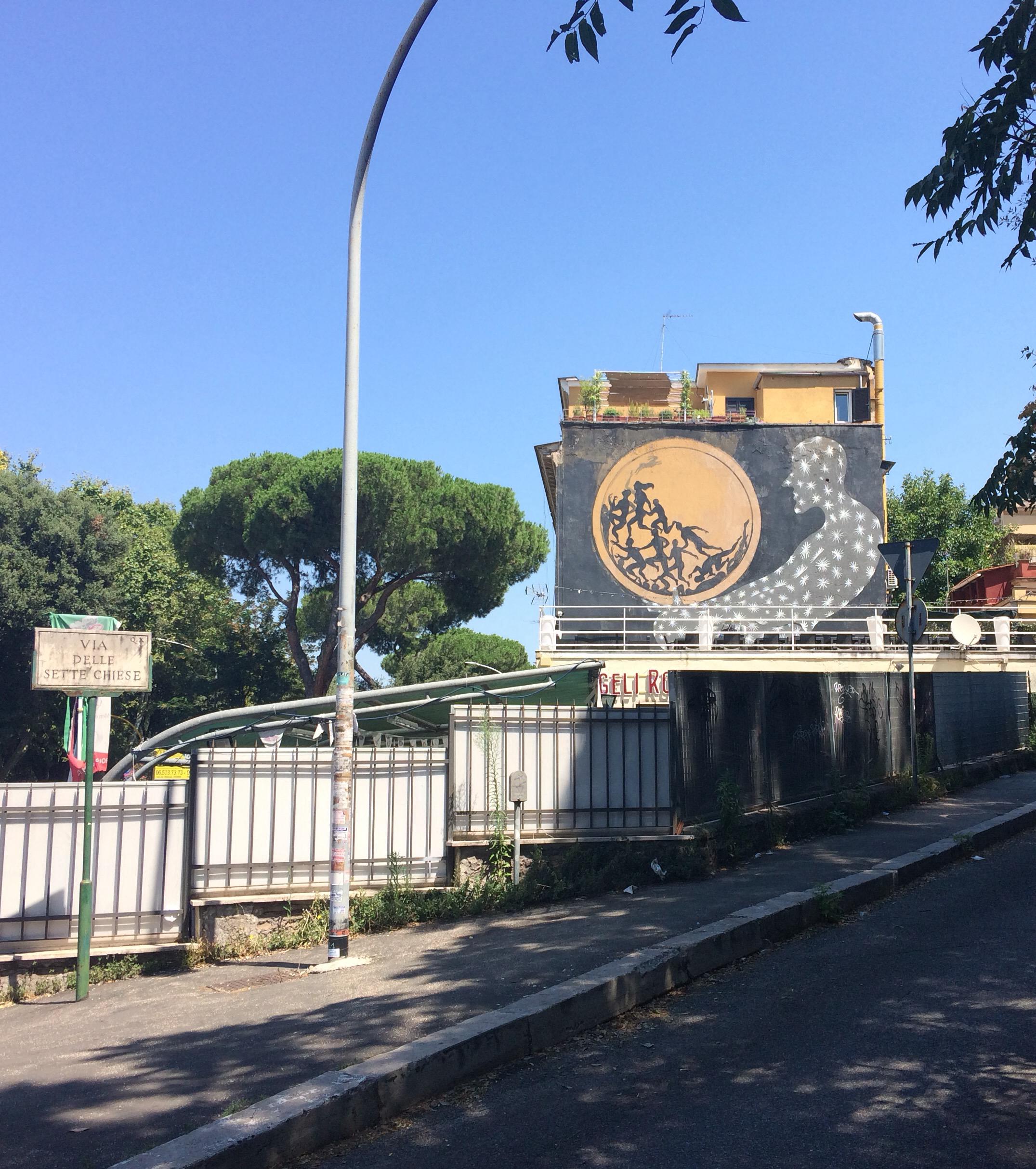 Small mural with a golden disc and a ghostly white figure above a roadside wall