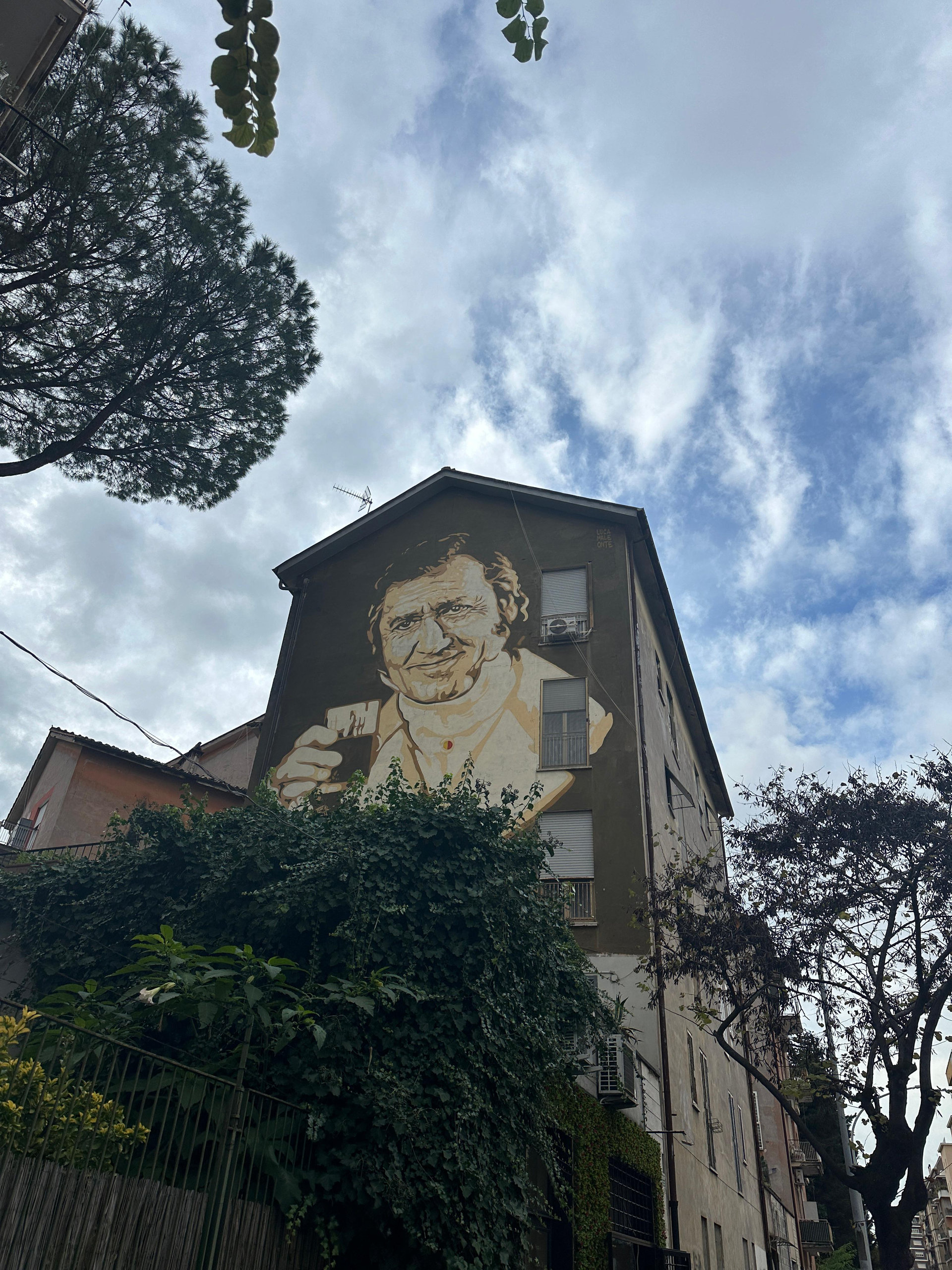 Large sepia mural of a smiling man holding a glass on the gable of an apartment building
