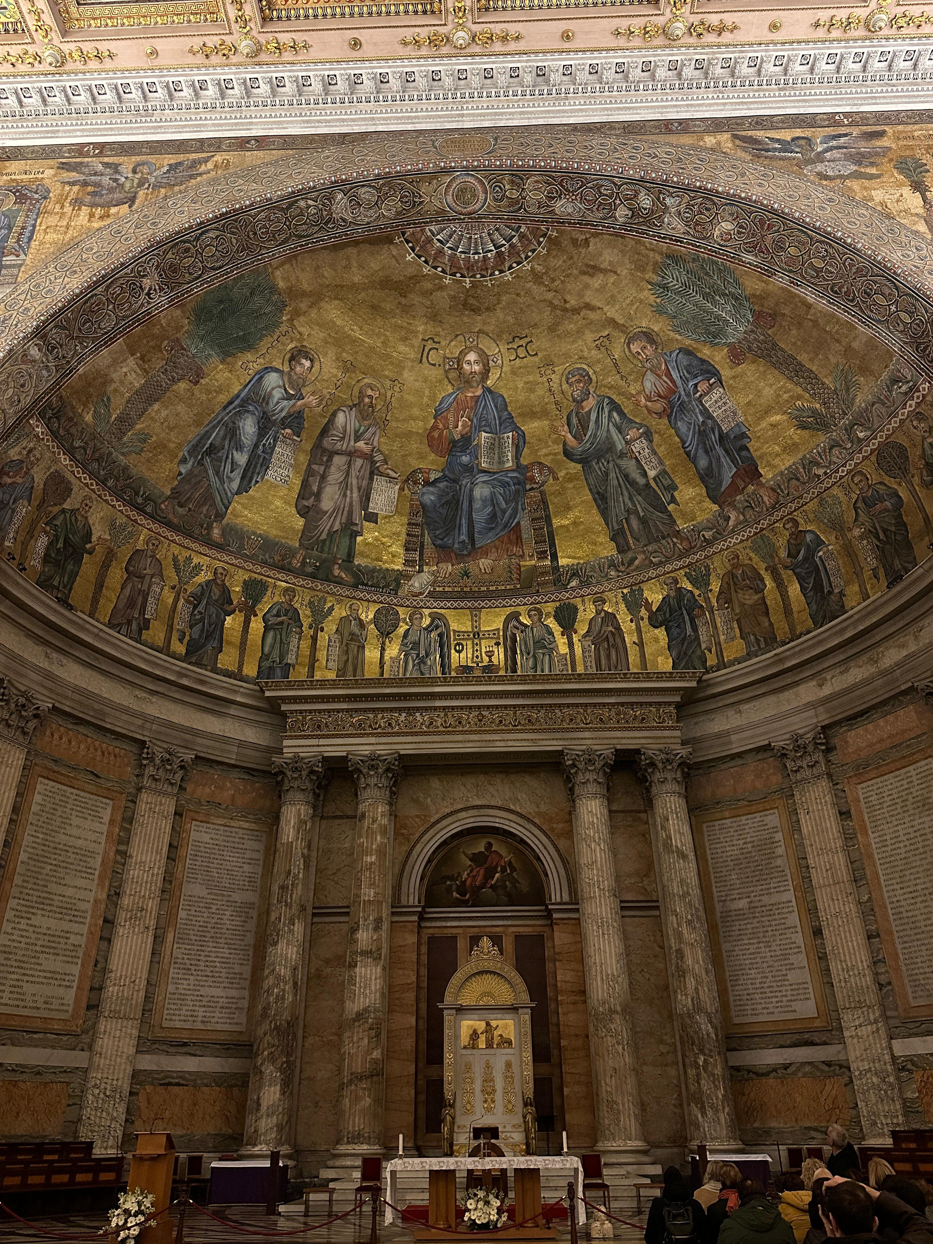 Golden apse mosaic of Christ enthroned with saints above a marble-lined basilica sanctuary