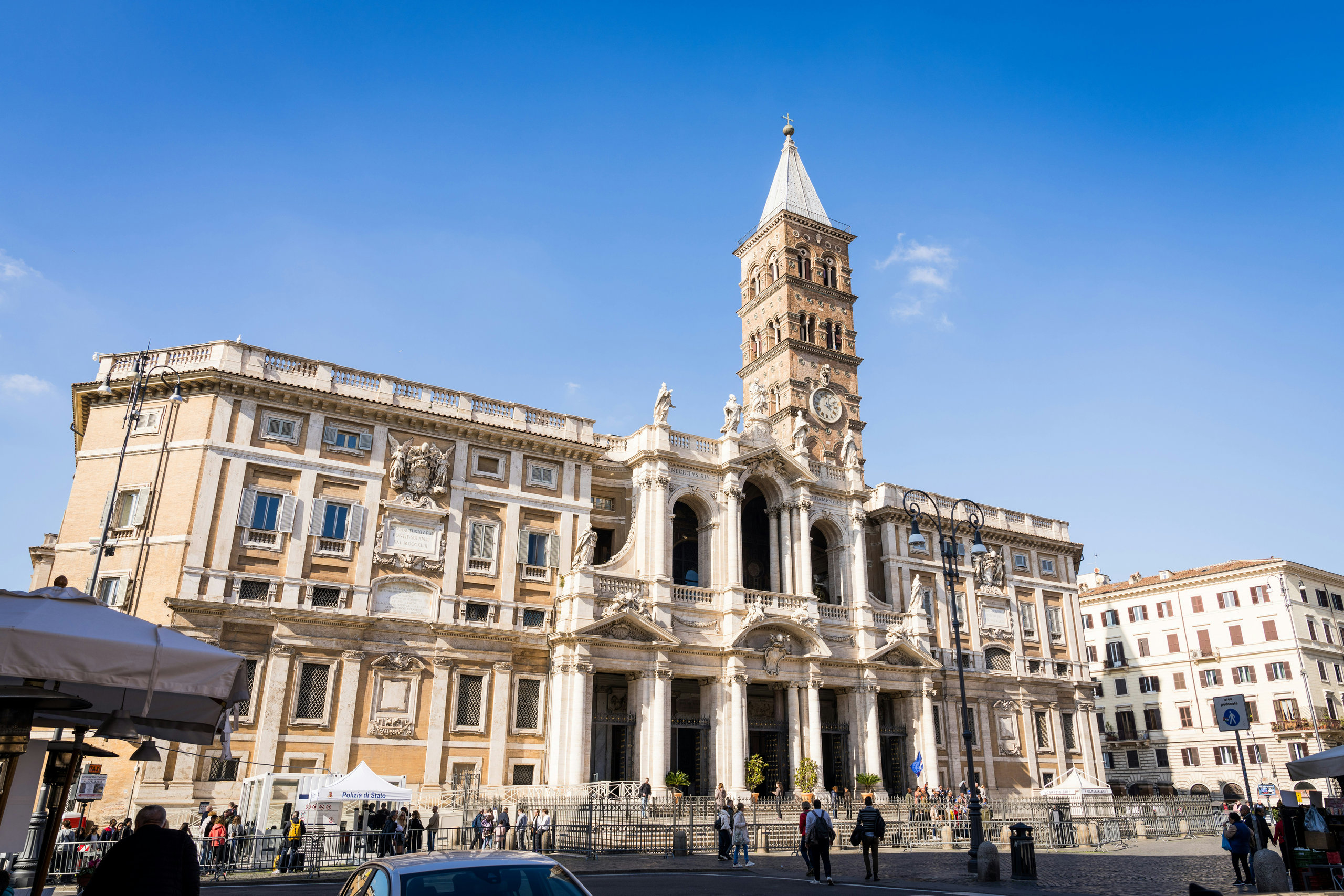 Baroque basilica with a tall bell tower and pale ochre facade on a sunny Roman square