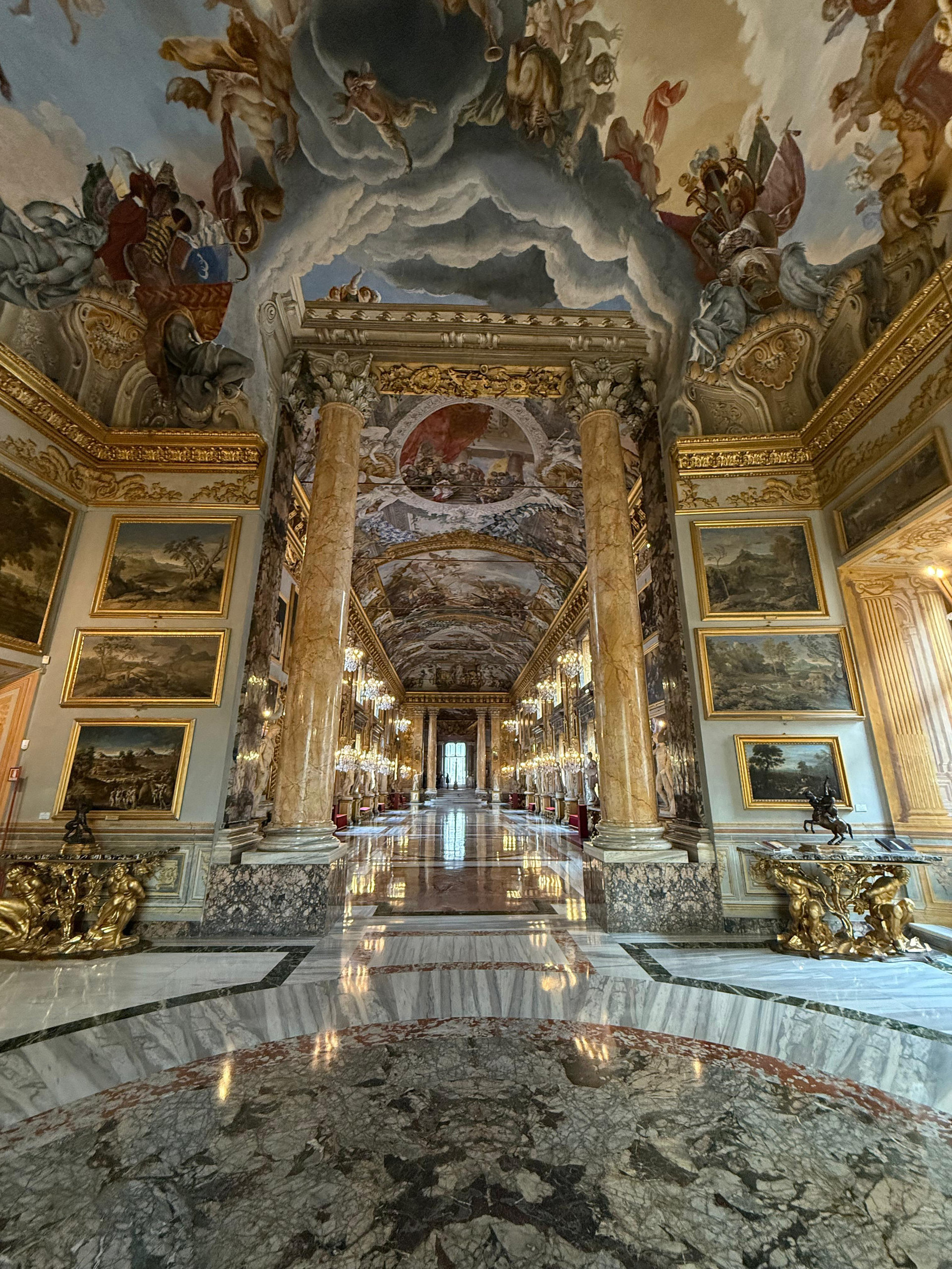 Perspective down a gilded hall of golden marble columns, chandeliers and frescoed ceilings