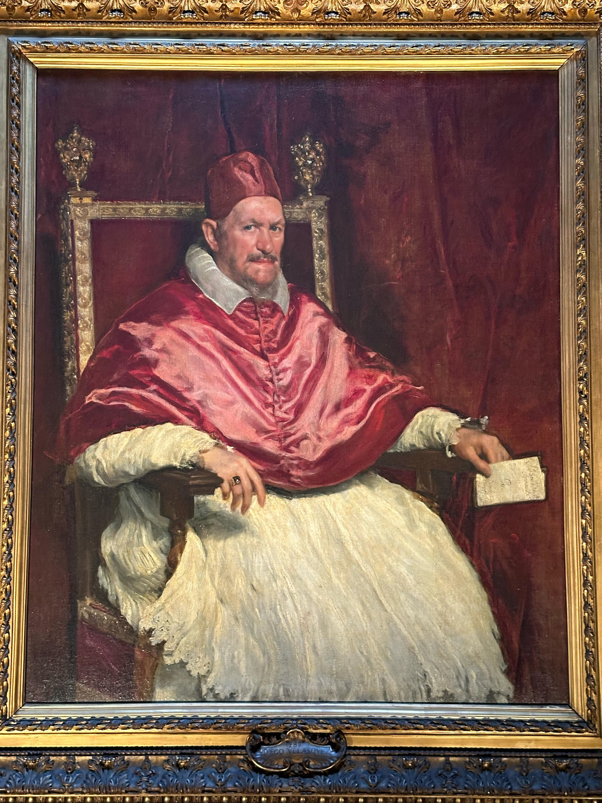 Portrait of a seated pope in red cape and white lace surplice in a gilded frame at Palazzo Doria Pamphilj