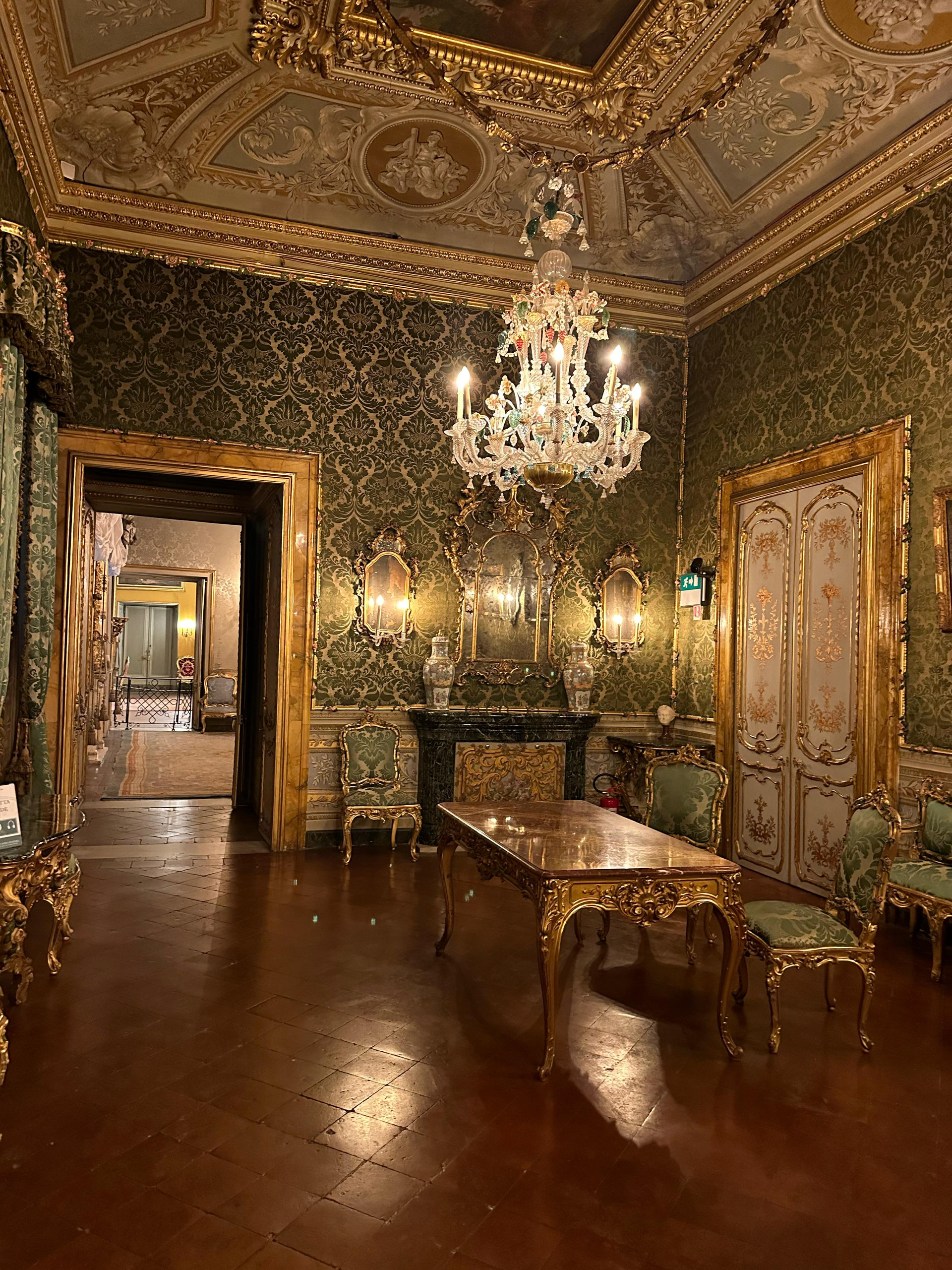 Green damask salon with a gilded table, chandelier and mirrors beneath a painted ceiling