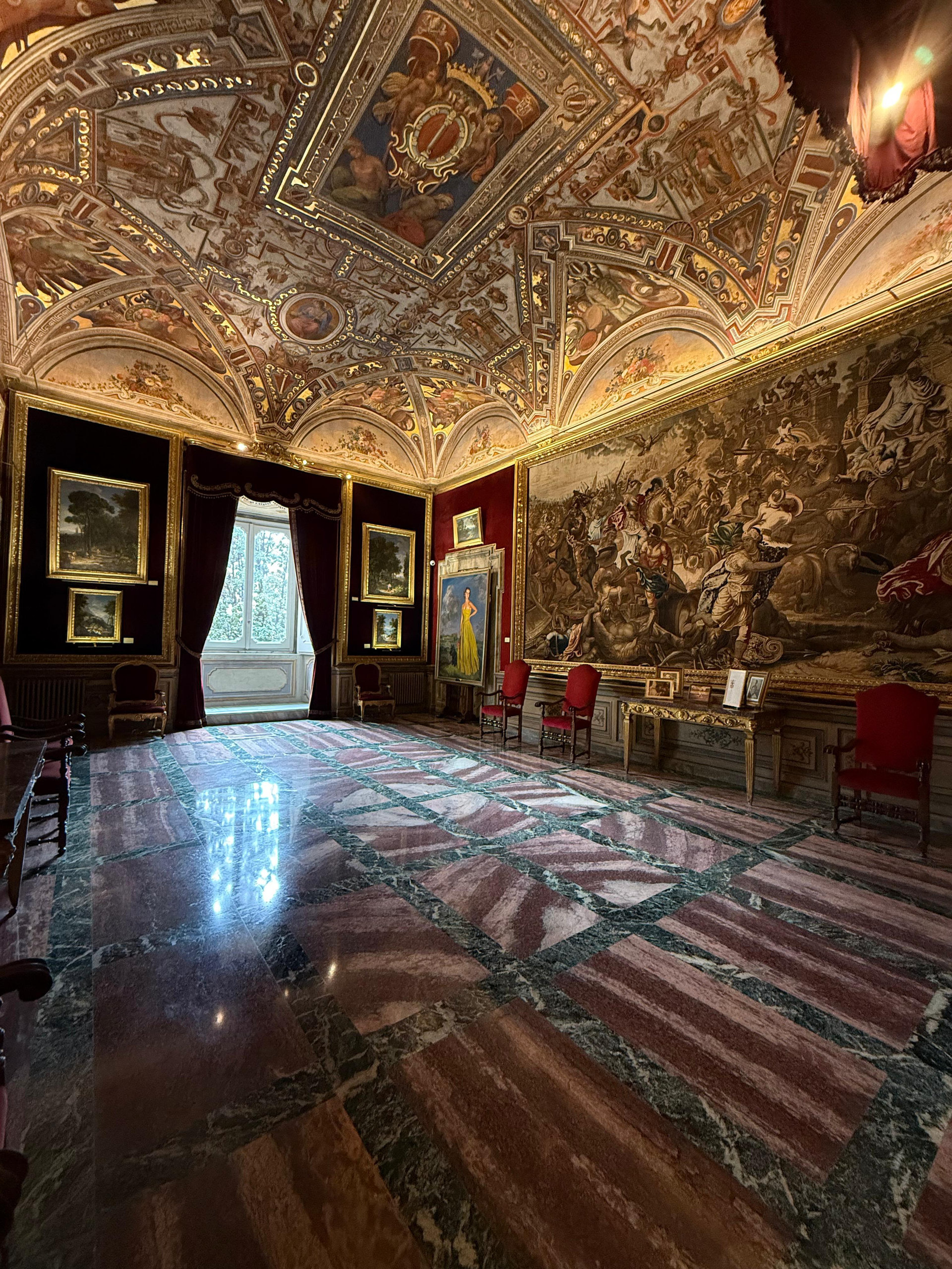 Room with a coffered painted ceiling, battle tapestry and pink marble floor