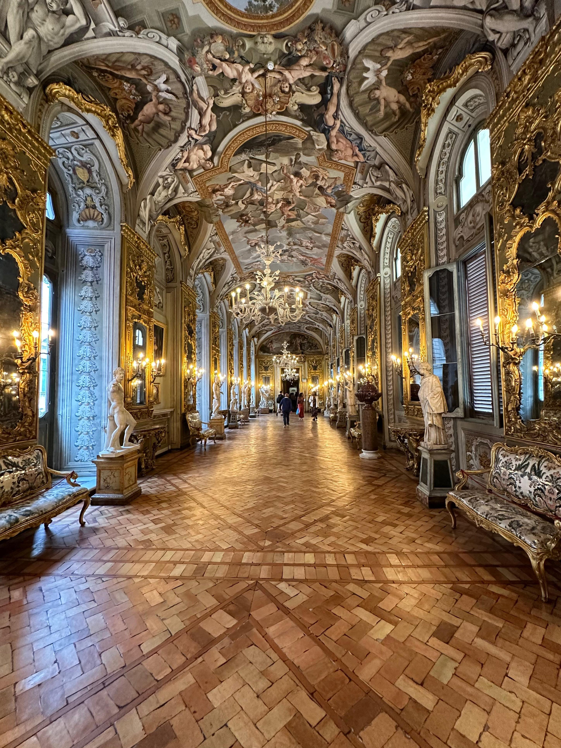 Long mirrored gallery with frescoed vaults, white statues and a patterned parquet floor