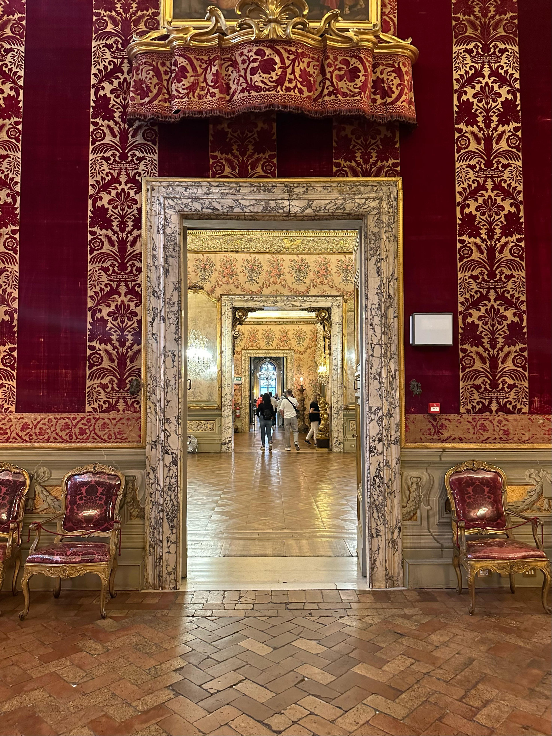 Marble doorway framing a view through red-velvet-walled rooms with gilded furniture