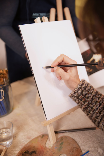 Hand sketching in pencil on a small canvas on a wooden tabletop easel