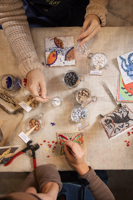 Overhead view of a mosaic workshop with jars of tesserae, tweezers and small finished mosaics