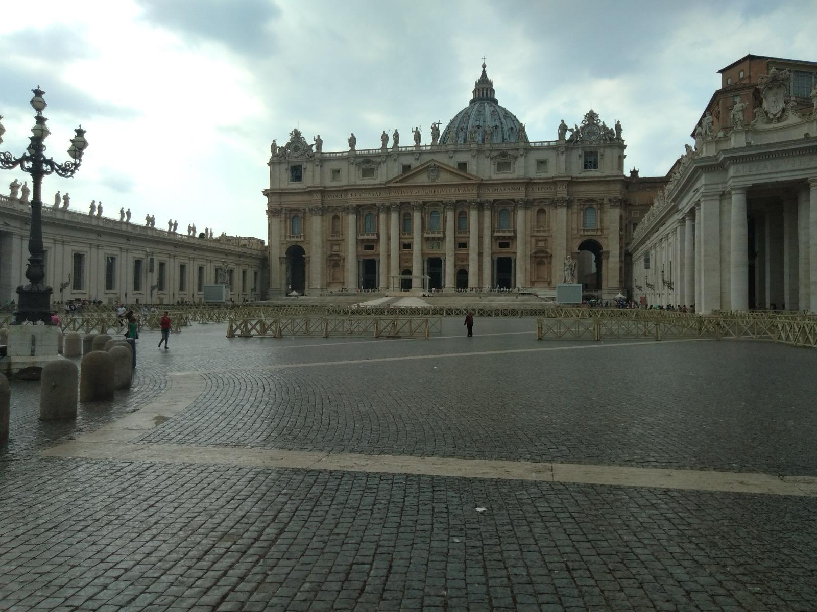 Facade of Saint Peter's Basilica across the wide cobbled square under a cloudy sky