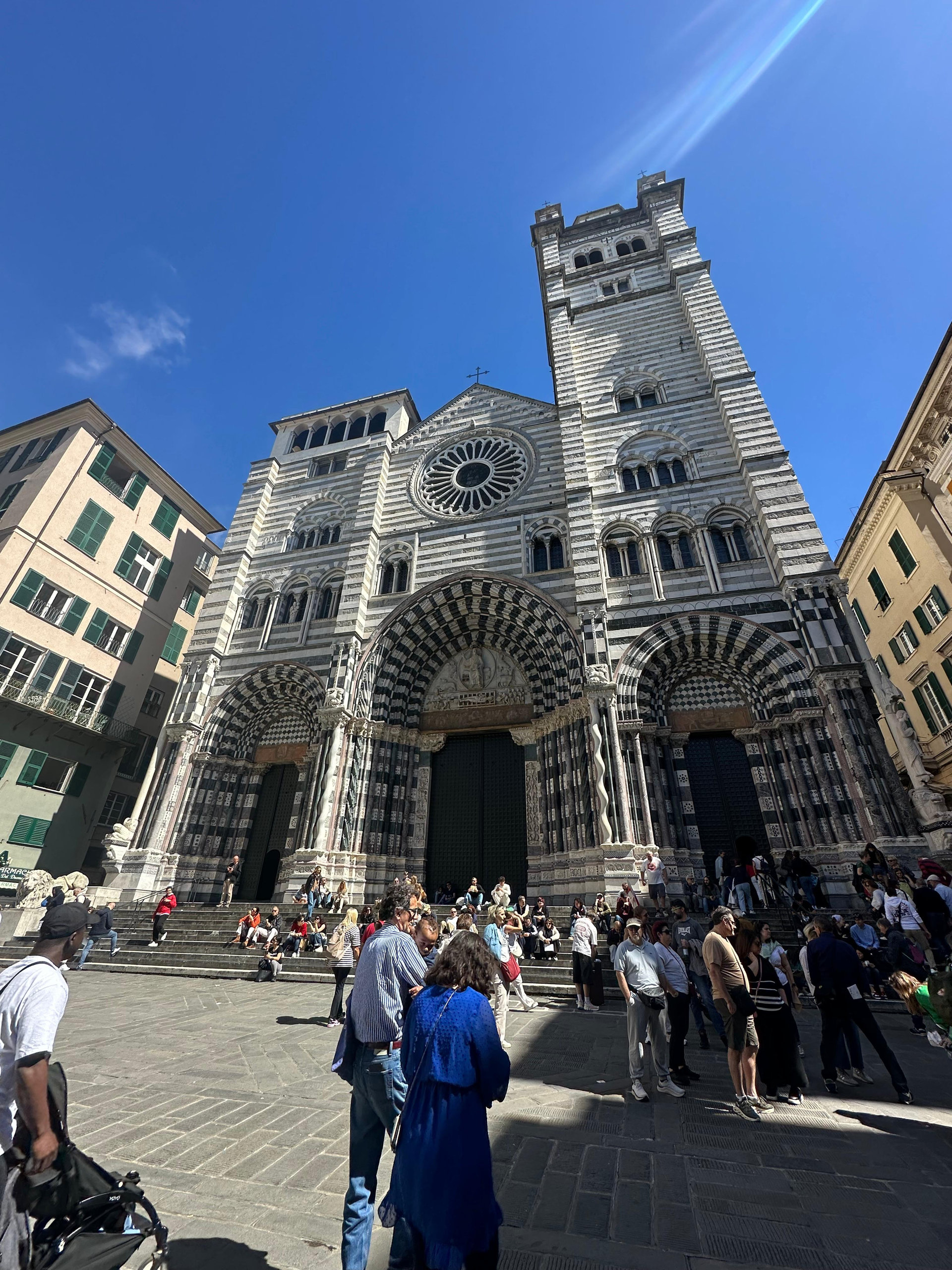 Striped black-and-white marble cathedral facade with a rose window and visitors on the steps