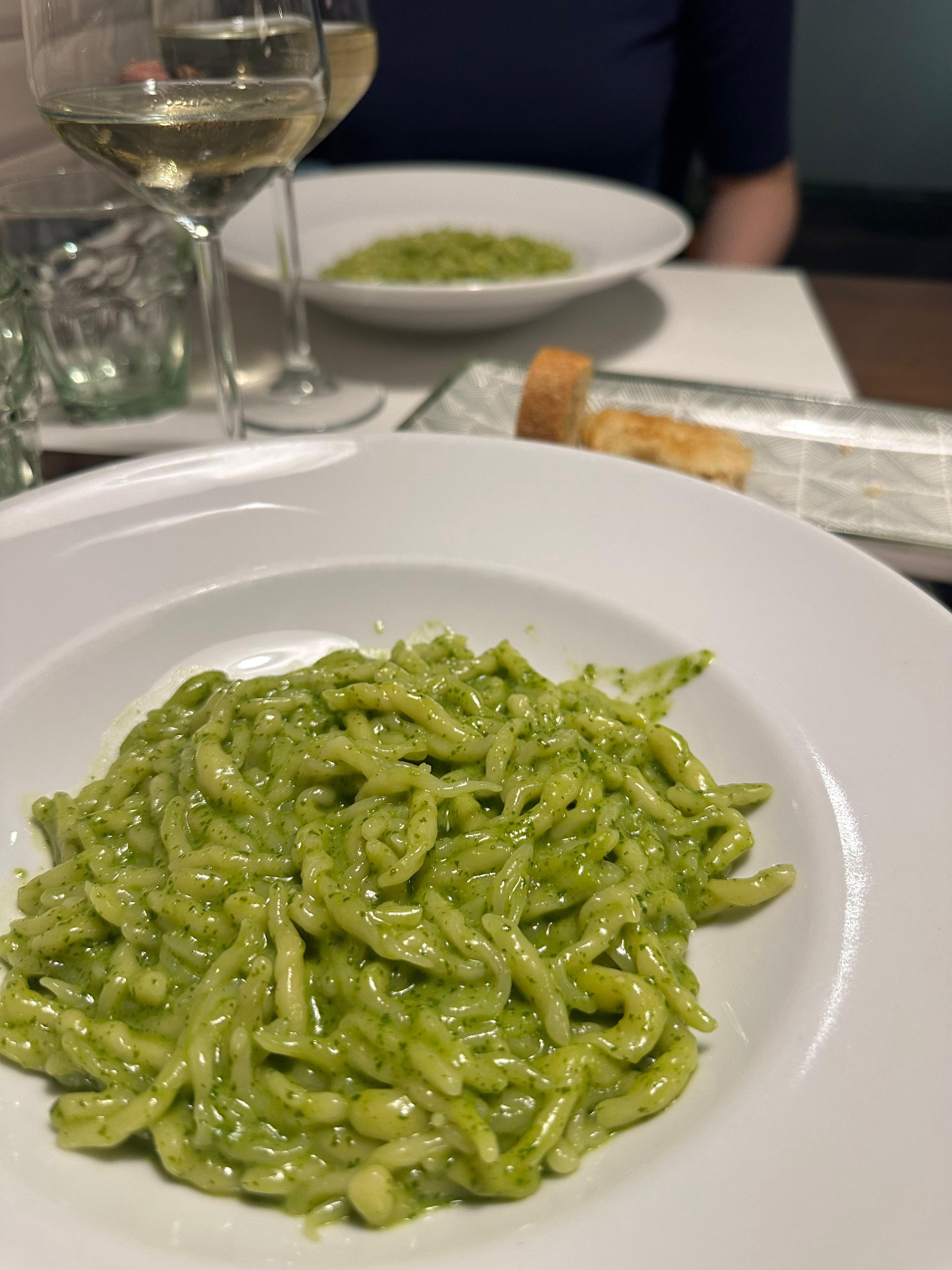 Plate of green pesto pasta with a glass of white wine on a restaurant table