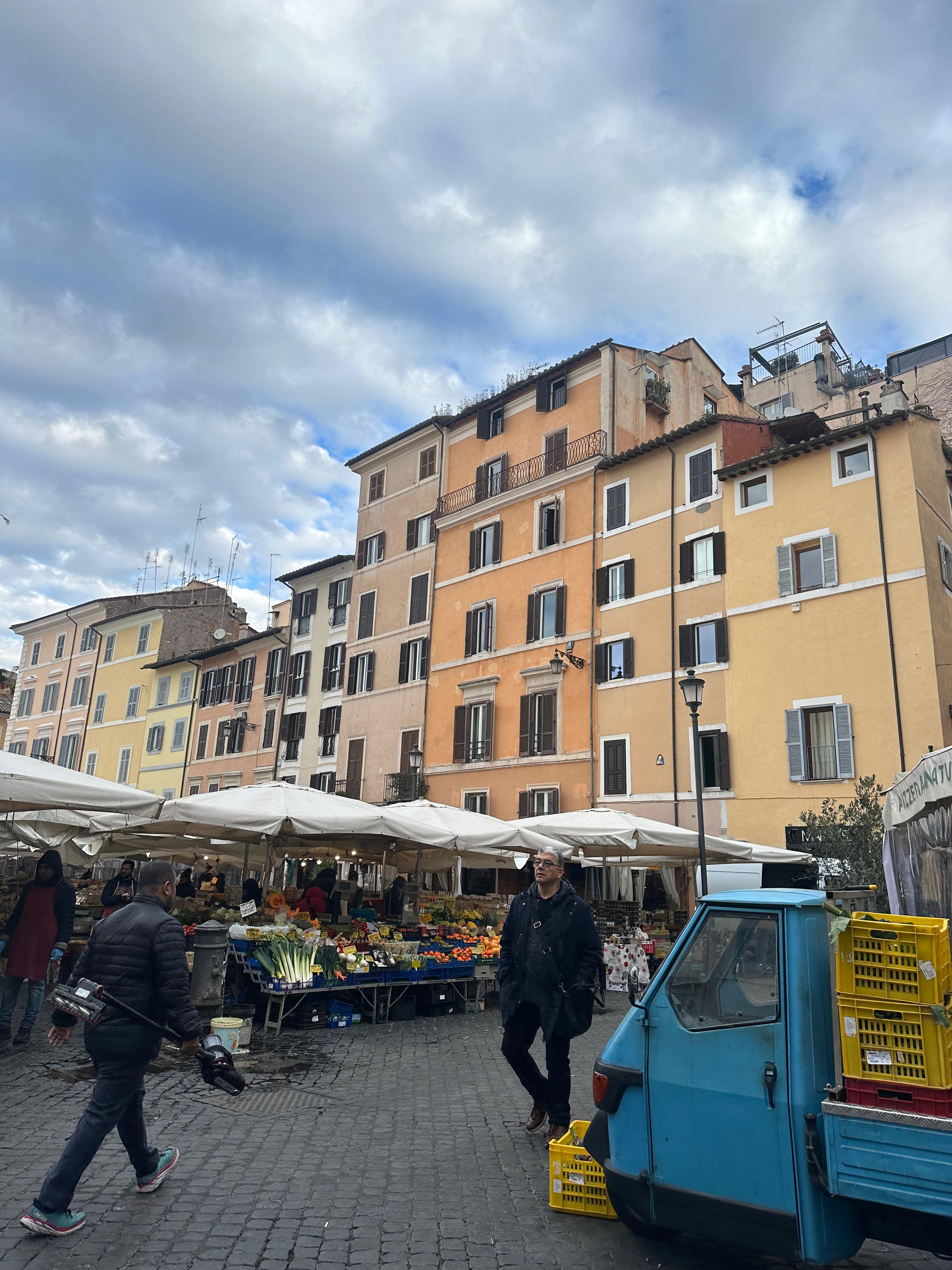 Campo de' Fiori in Rome with ochre buildings, market stalls and a small blue three-wheeler truck