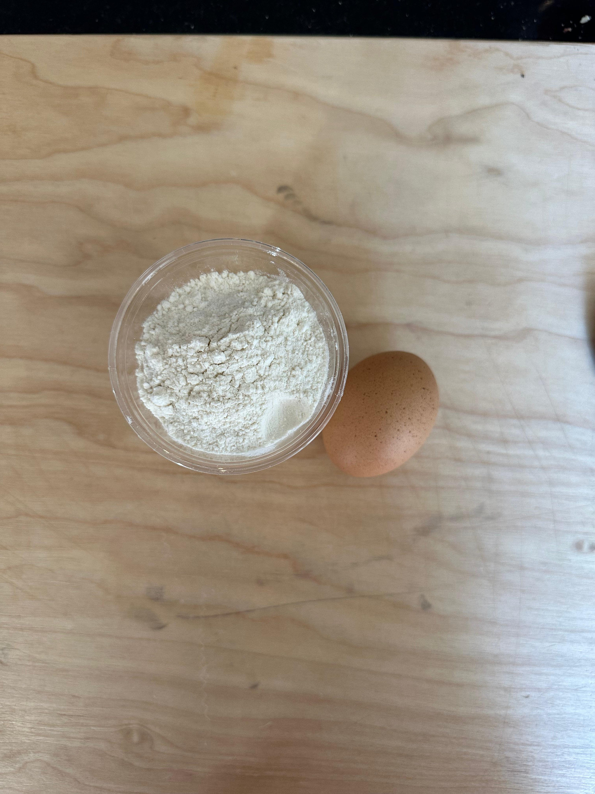 Small bowl of flour and a brown egg on a wooden board, ready for making pasta
