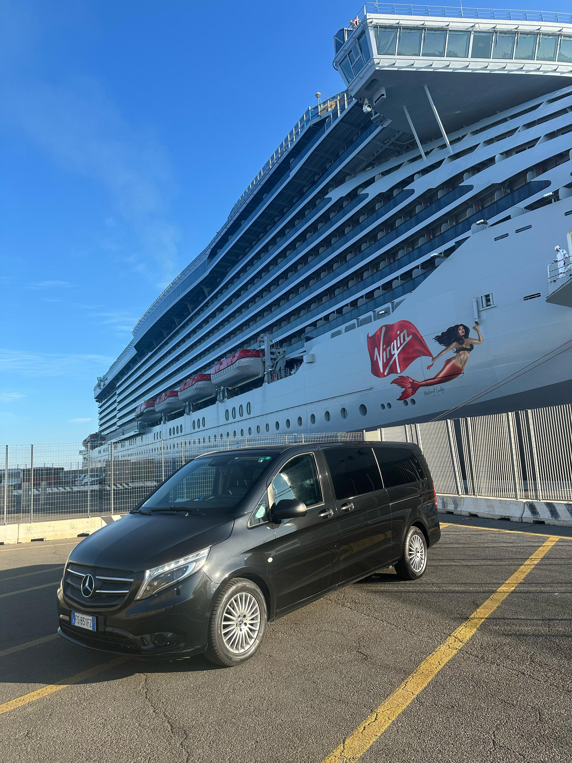 Black private minivan parked at the port in front of a huge cruise ship