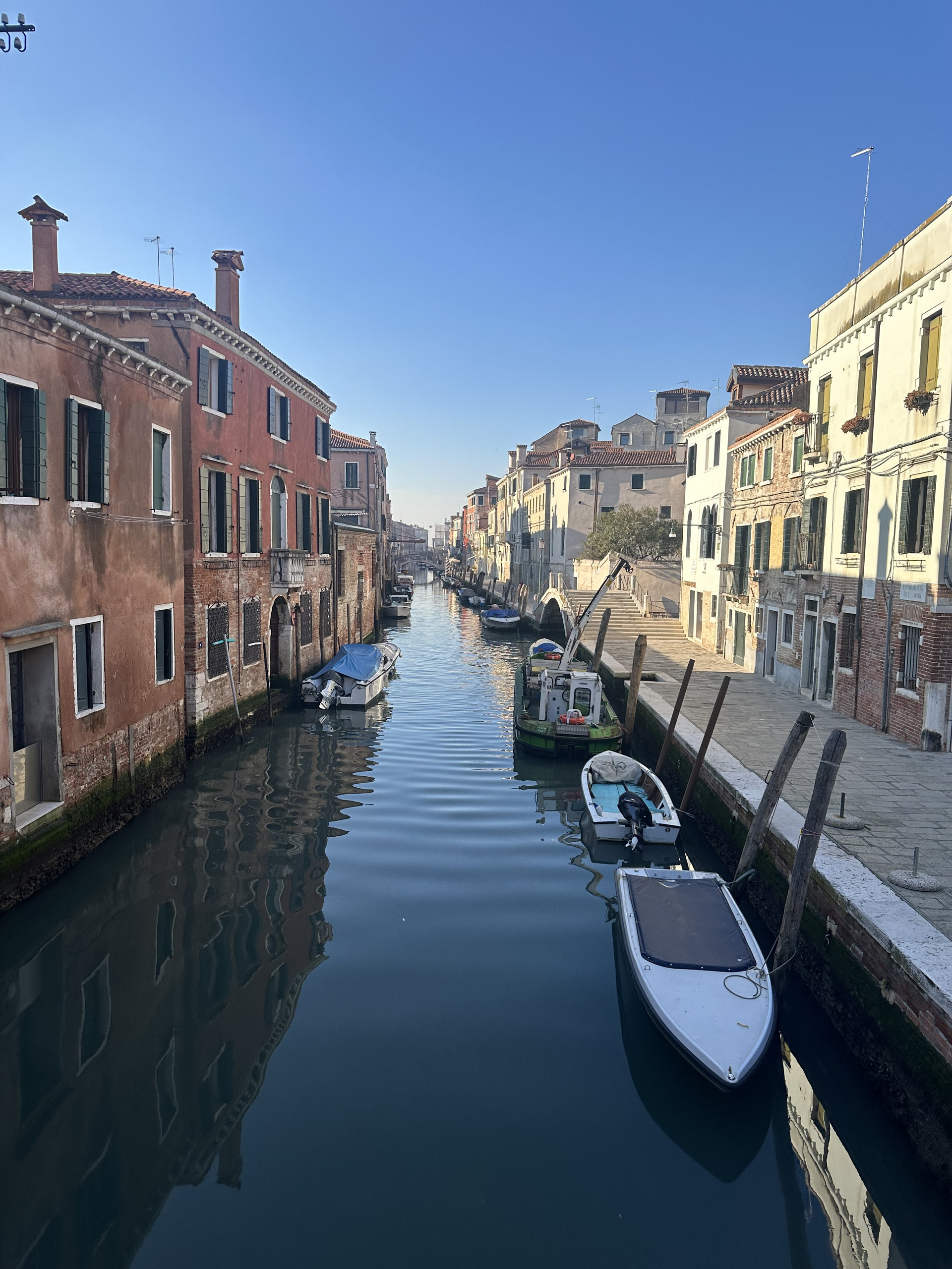 Quiet Venetian canal lined with pastel houses and small boats in clear morning light