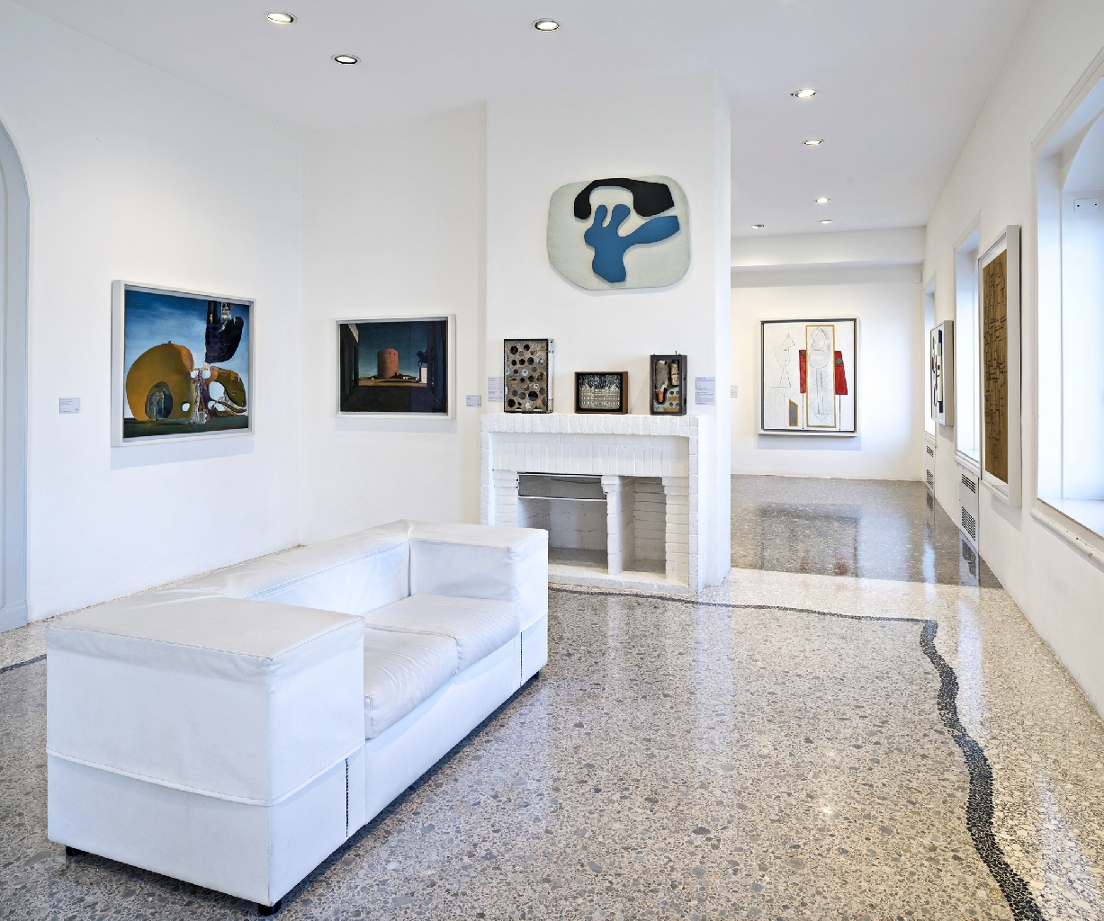 Bright modern gallery room with a white sofa, a fireplace and abstract paintings on the walls