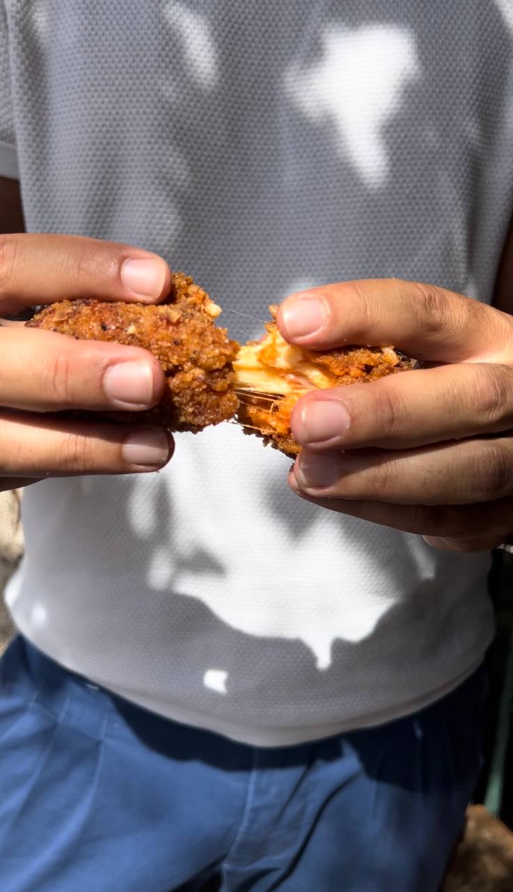 Hands pulling apart a fried rice croquette with melted cheese stretching inside
